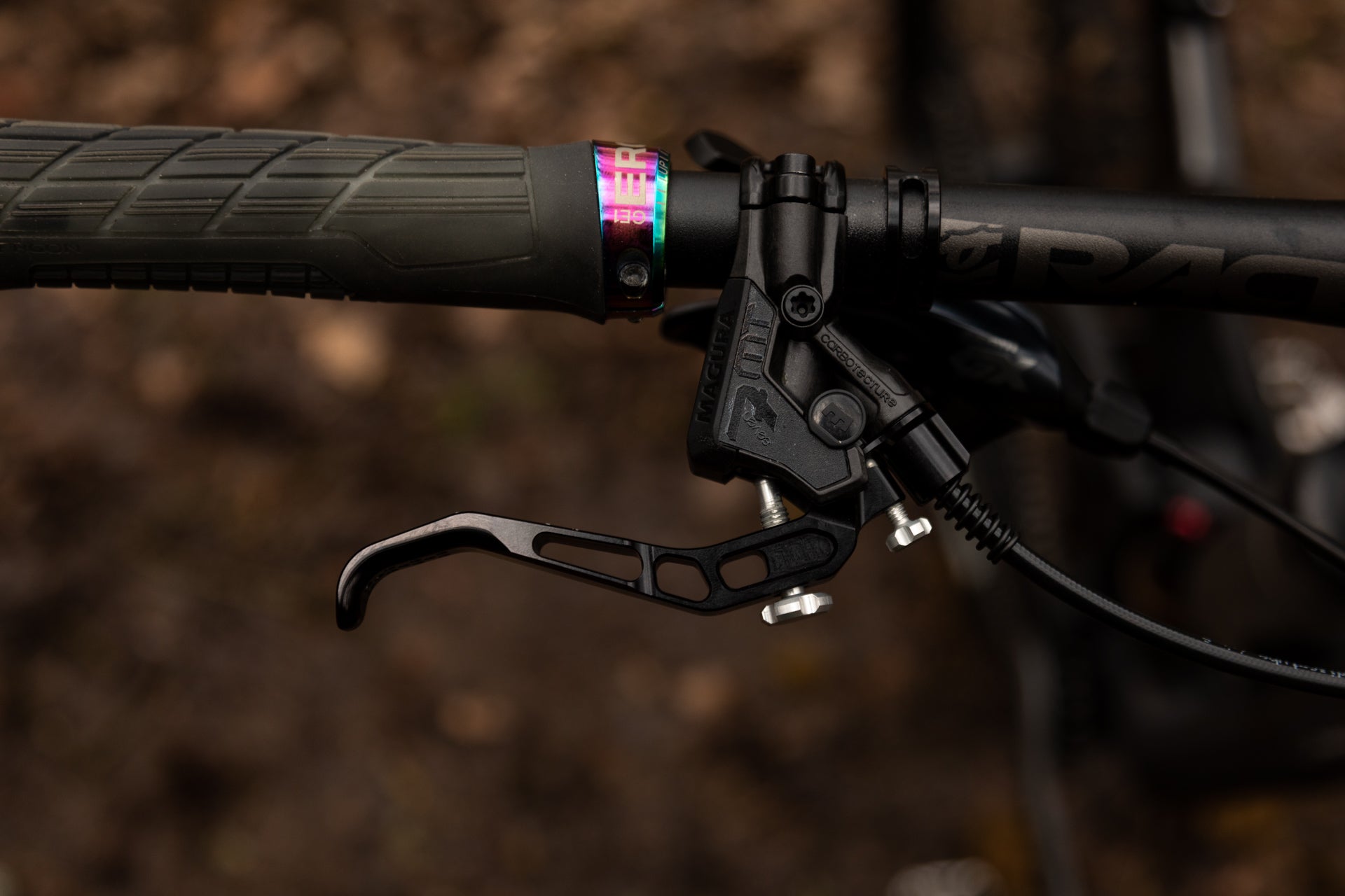 Close-up of black MAGURA CORBOTE mountain bike brake lever and rubber grip on handlebar, outdoor background.