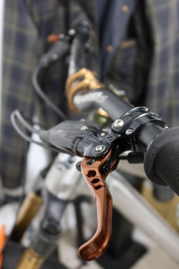 Black bicycle handlebar grip with copper brake lever and bolts, showcasing ergonomic mountain bike design.