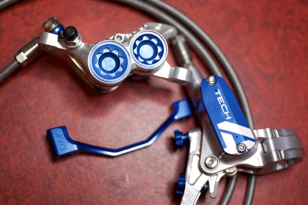 Blue and silver hydraulic mountain bike brake system with TECH lever and caliper on a red surface.