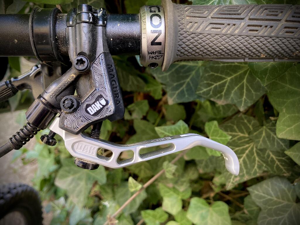 Close-up of a mountain bike handlebar with MAGURA DAK brake lever and textured GON throttle grip.