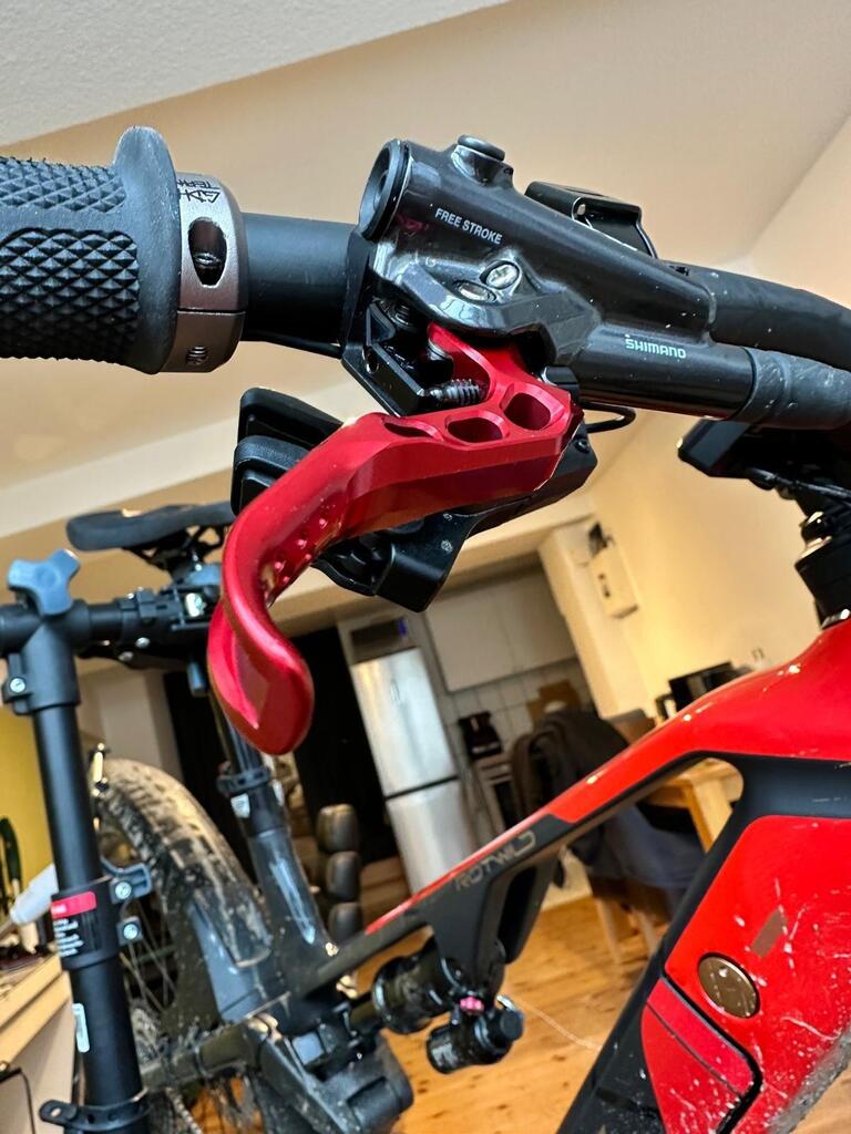 Close-up of a red mountain bike brake lever with 'FREE STROKE' and 'SHIMANO' branding on a black grip handlebar