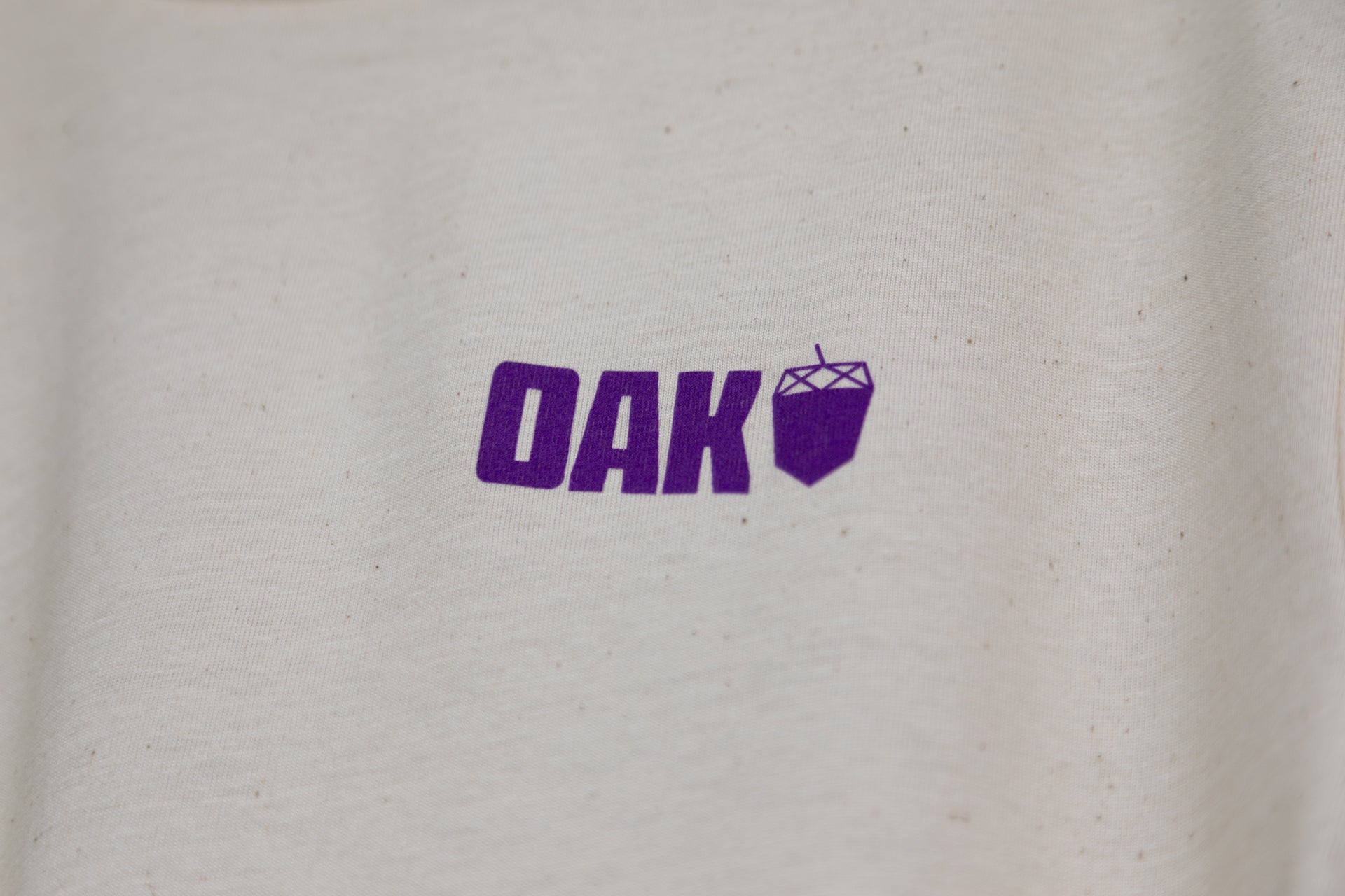 Close-up of beige fabric with purple DAK logo and geometric nut icon on mountain biking t-shirt