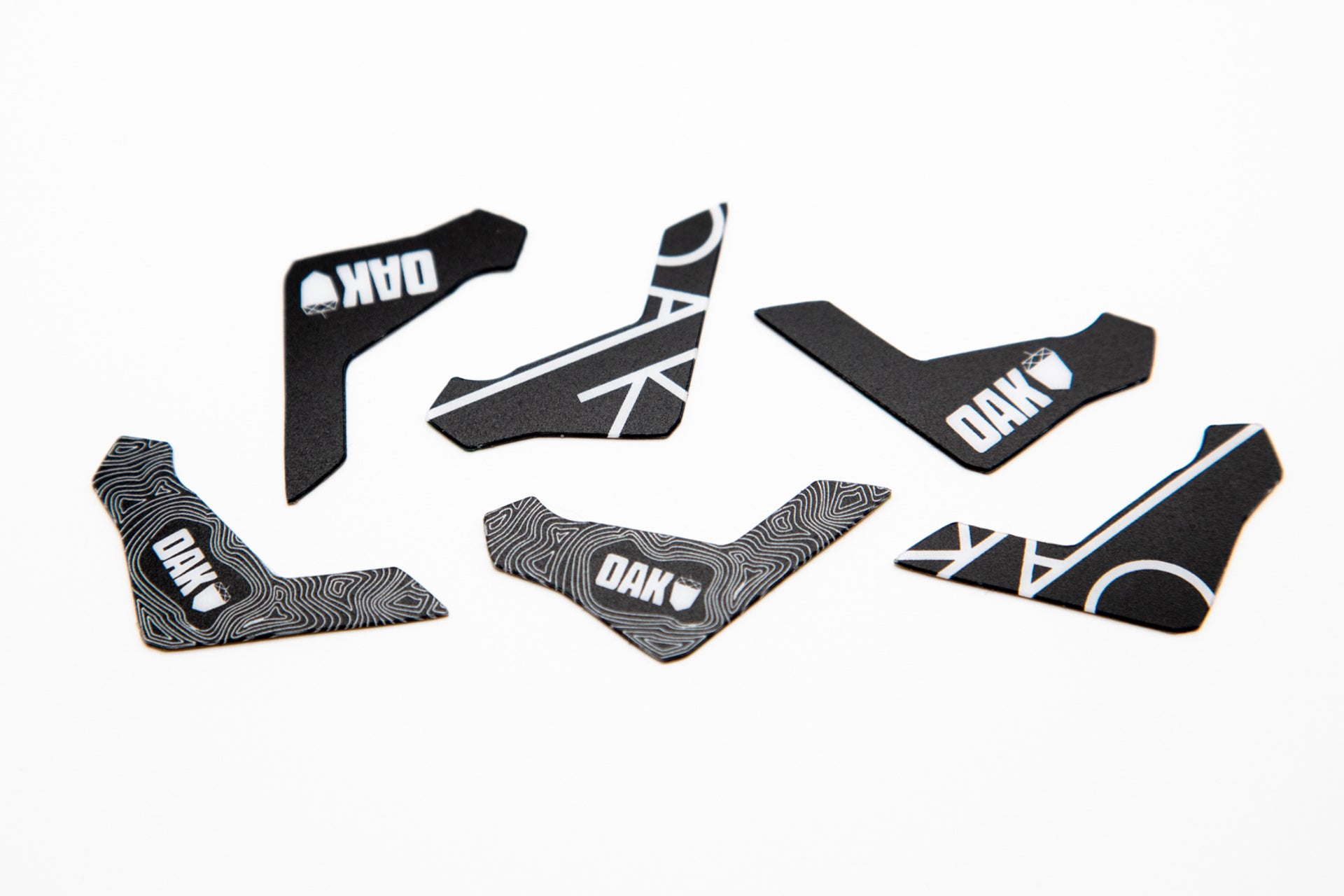 Set of six black adhesive patches with white OAK and DAK text and contour designs on whit background.