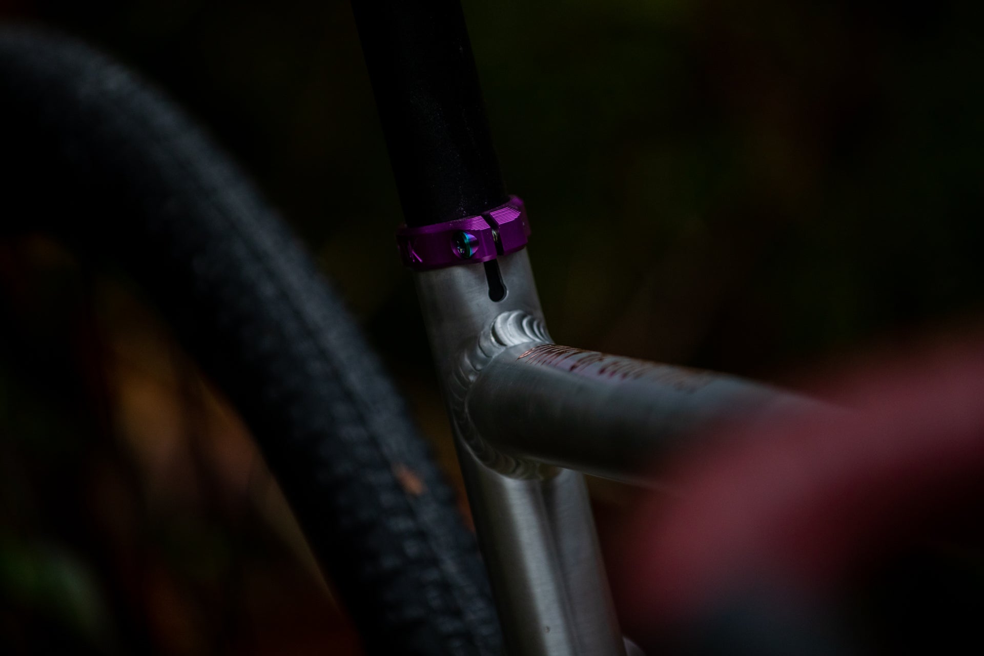 Close-up of a silver mountain bike frame with welds and a purple seat post clamp, tire blurred in background