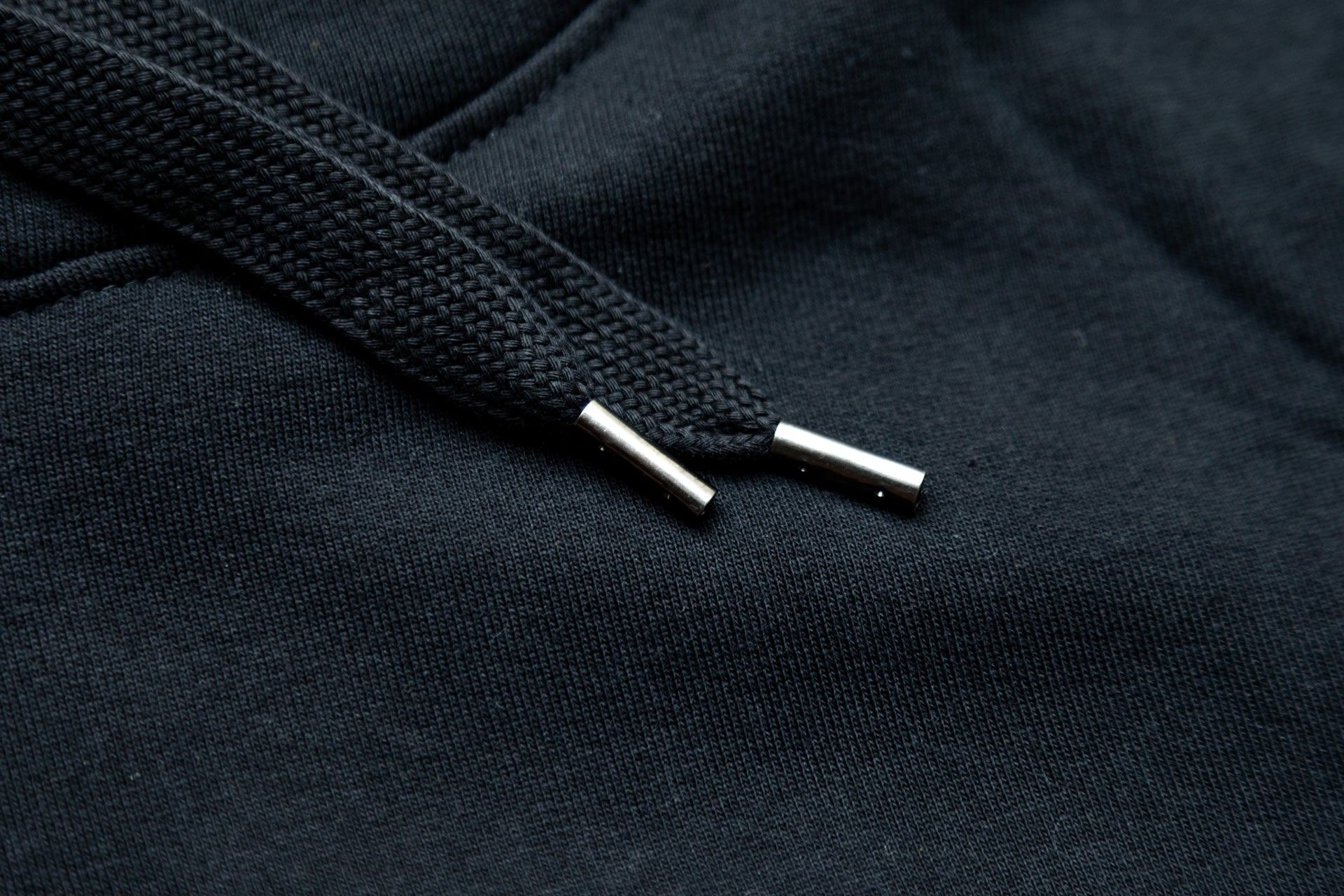 Close-up of black braided drawstring with metallic aglets on textured black fabric.