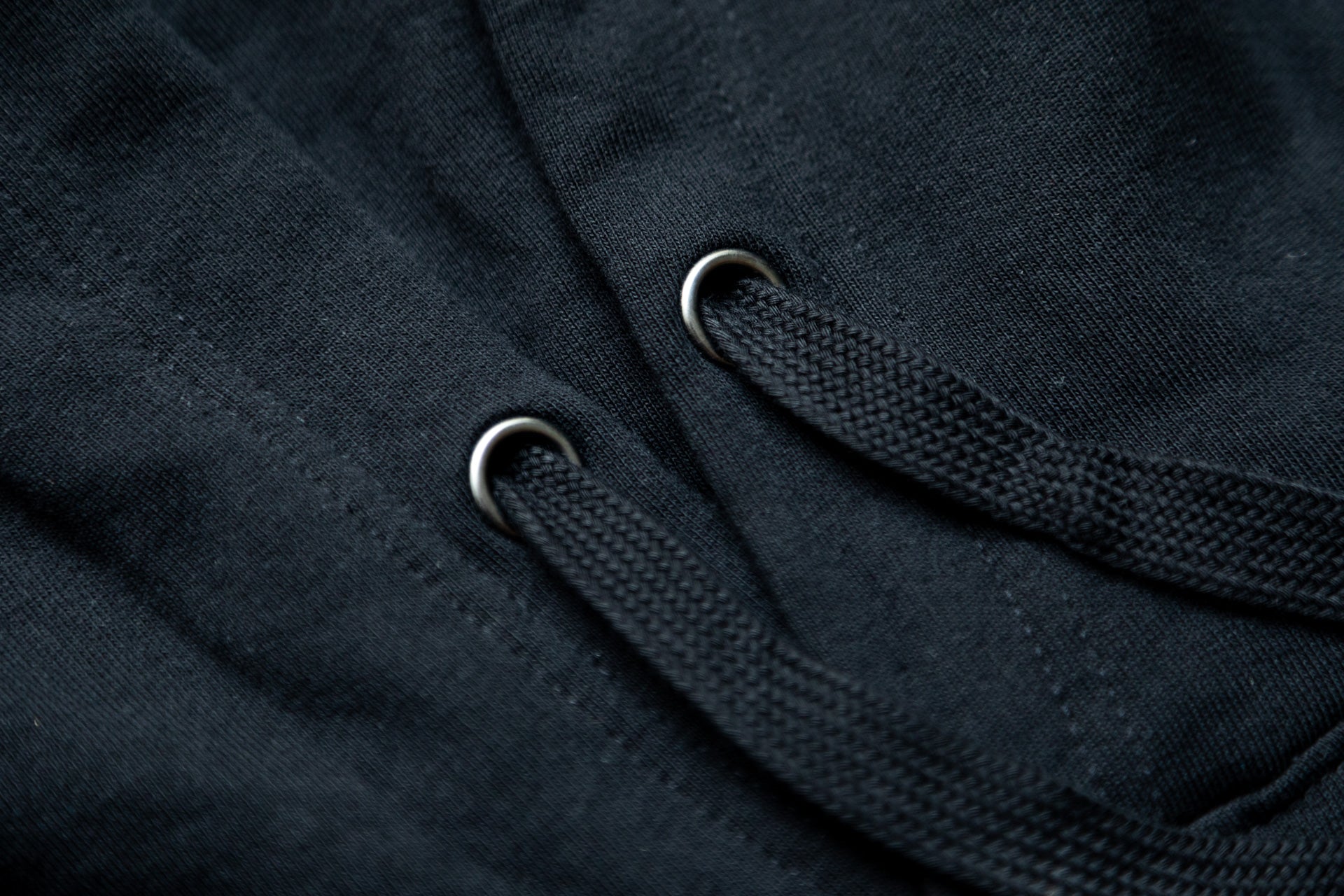 Close-up of black textured fabric with thick drawstrings through metal eyelets on a garment