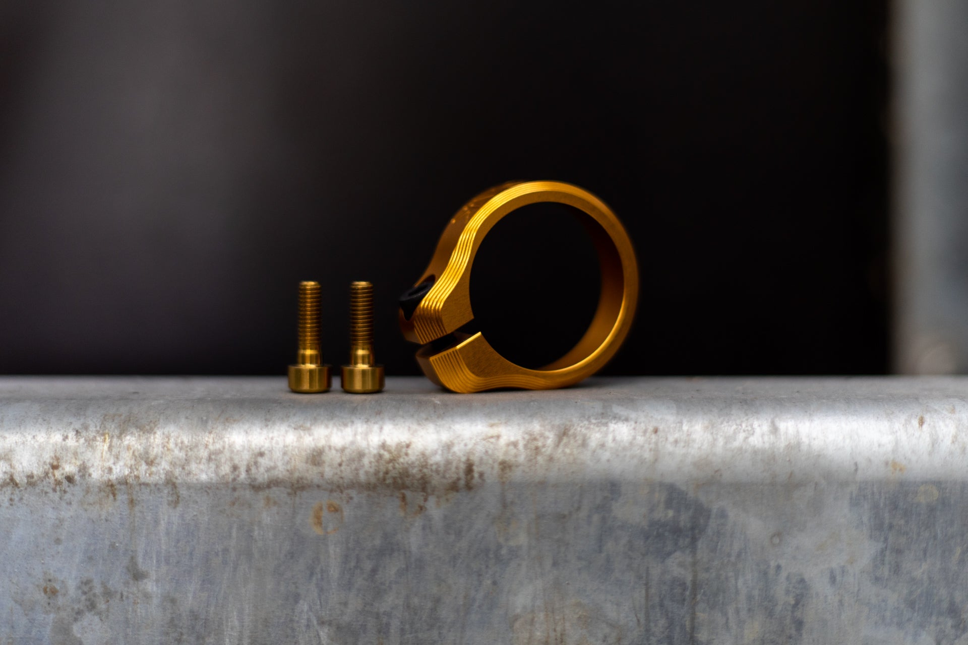 Gold metal ring clamp with textured surface and threaded bolts on grey metal base.