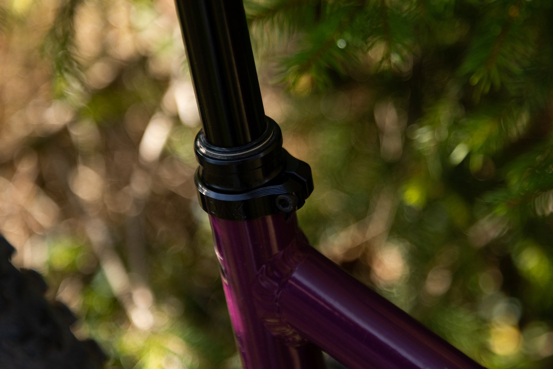 Close-up of a purple mountain bike seat tube with a black seat post and clamp beside the rear tire outdoors