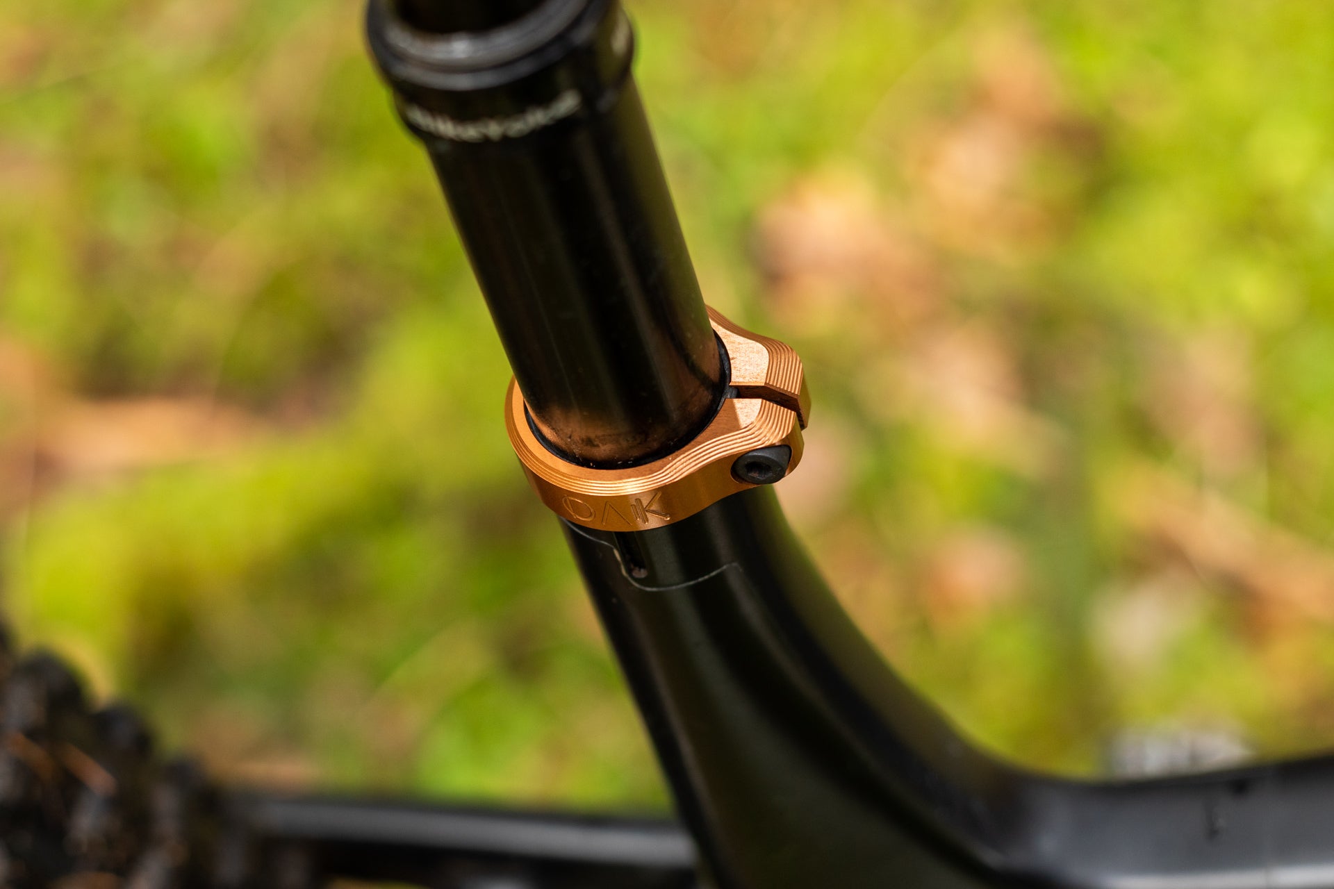 Close-up of a black bicycle seat post with an orange metallic OAK clamp and black bolt on a black frame.