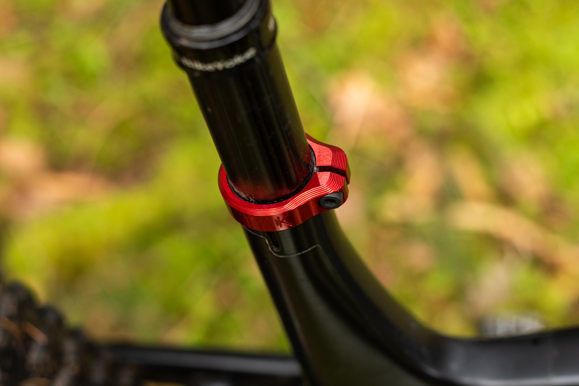 Black bicycle seatpost secured by a red metallic OAK clamp ring with engraved logo, mounted on a matte black frame