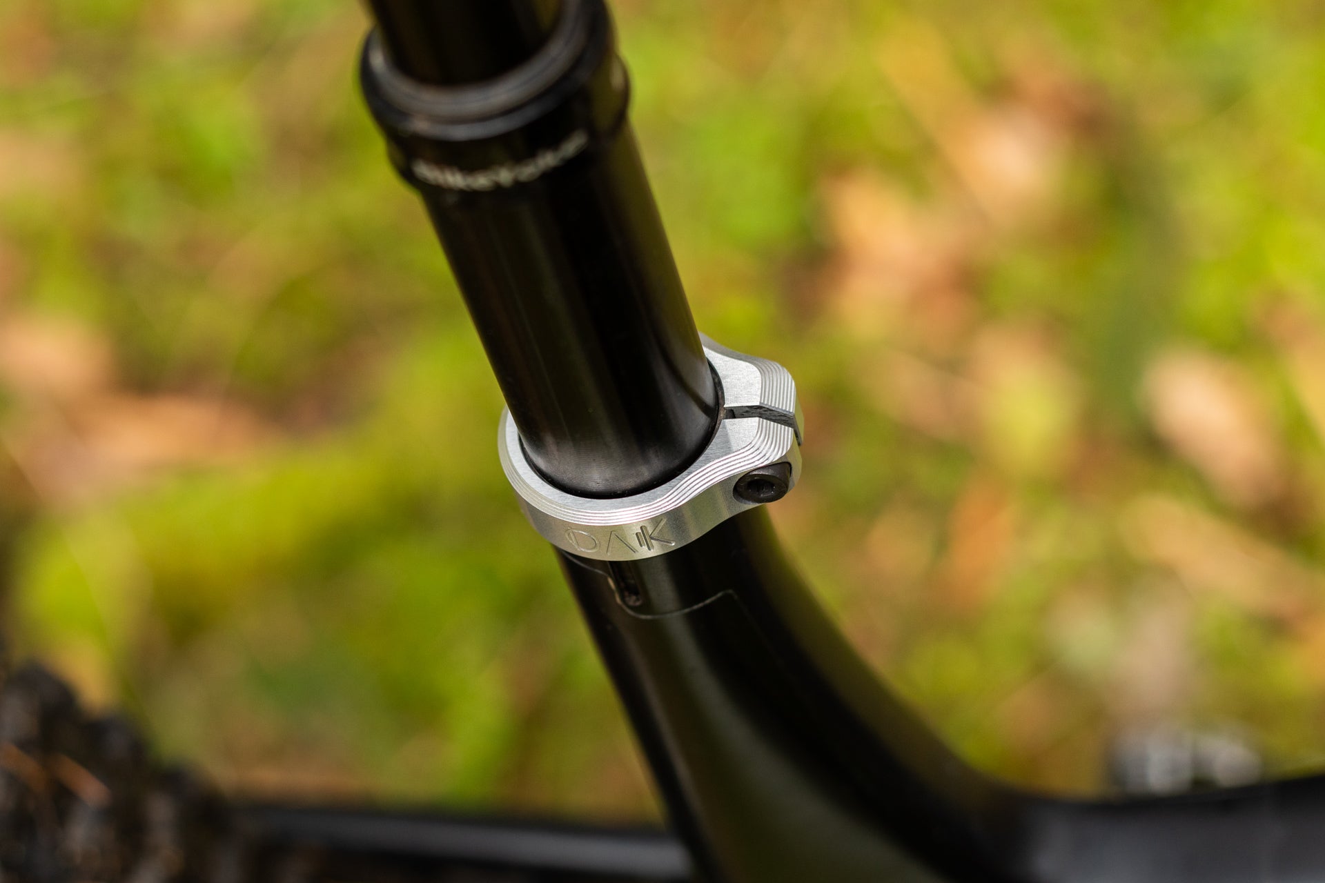 Black bicycle seat post with silver OAK seat clamp in a natural green and brown setting