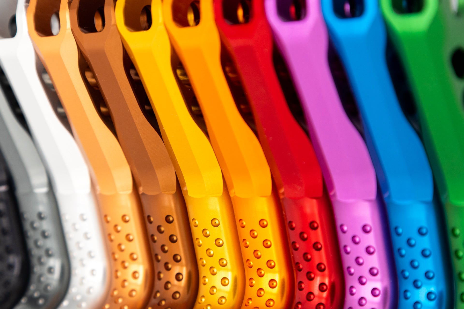 Close-up of colorful mountain bike carabiners with textured grips, displaying a gradient from dark to bright colors.