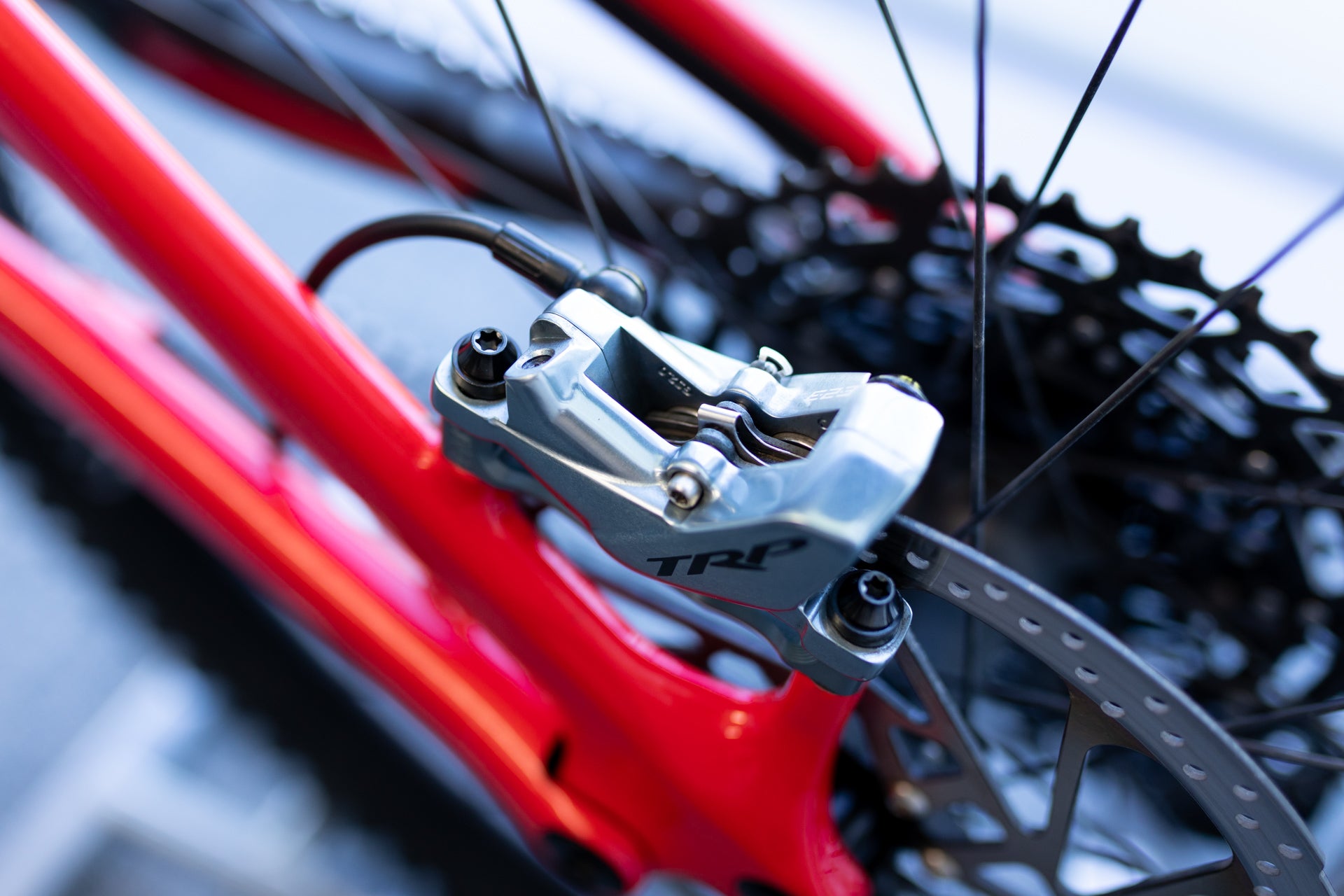 Close-up of TRP metallic rear disc brake caliper on red mountain bike frame with perforated brake rotor.