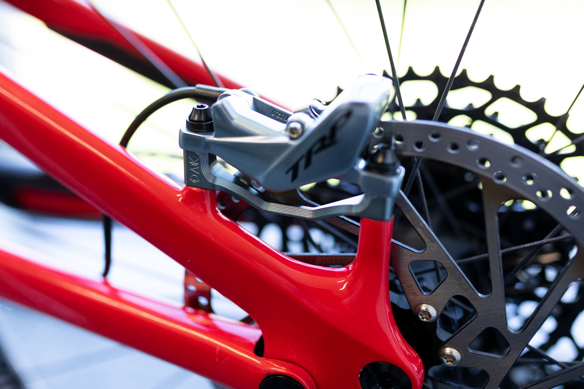 Close-up of a red mountain bike frame with a silver PMK brake caliper on a disc brake rotor and black spokes.