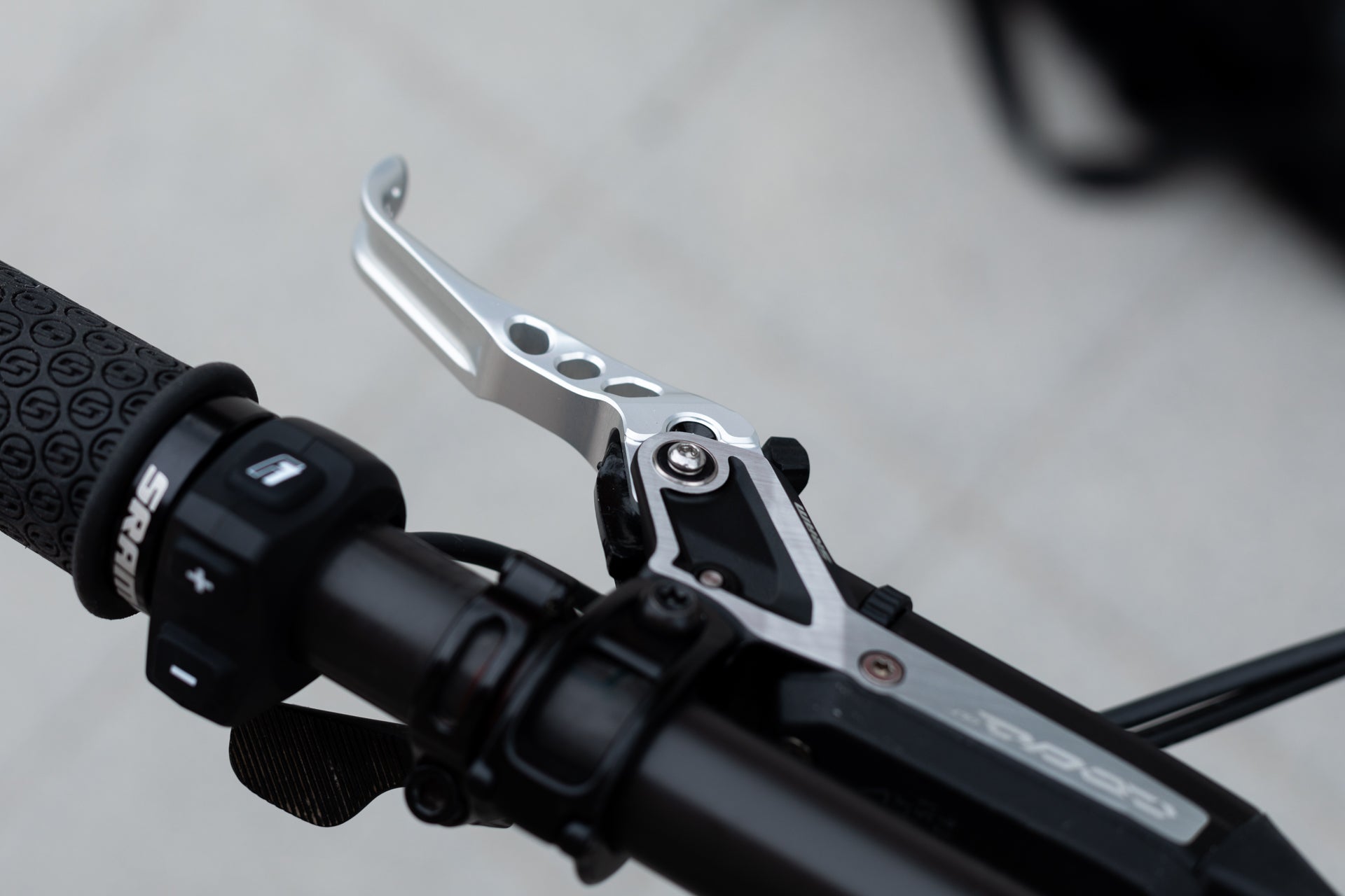 Close-up of mountain bike handlebar with textured grip, silver brake lever with holes, and 'SRA' control switch.