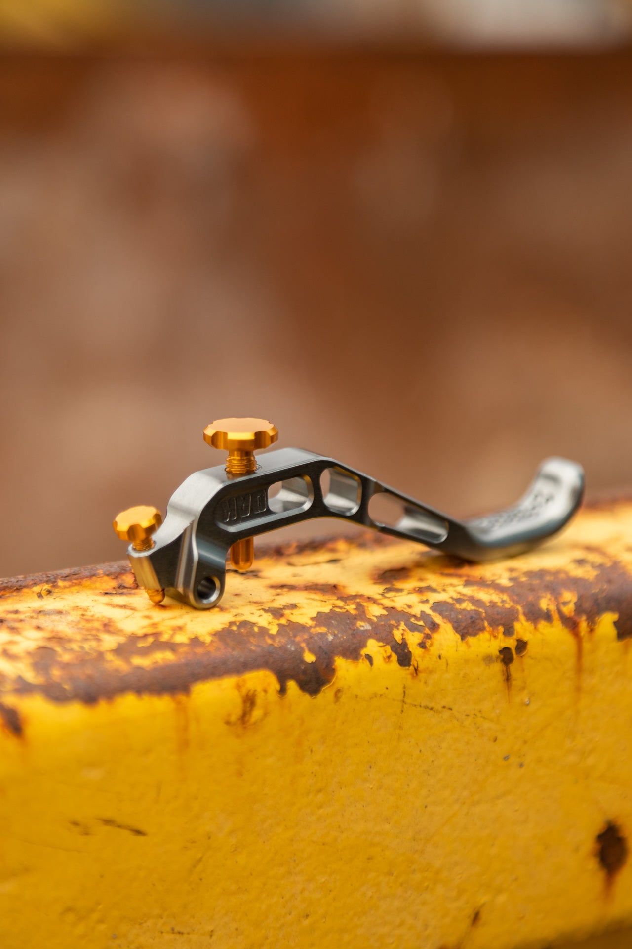 Metallic mountain bike lever with orange adjustment screws and WD engraving on textured yellow surface