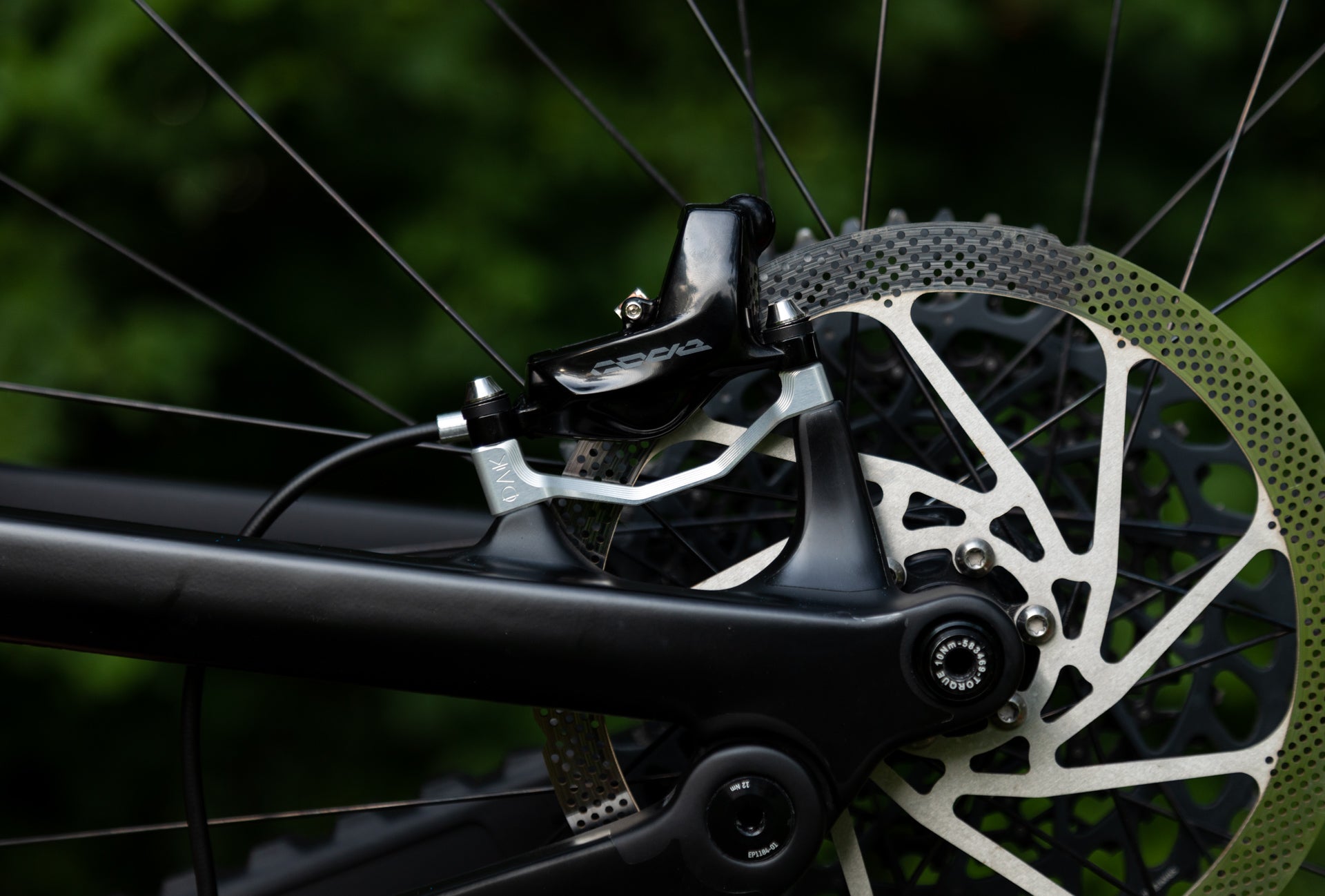 Close-up of OAK black and silver bicycle disc brake caliper and ventilated rotor on matte black frame.