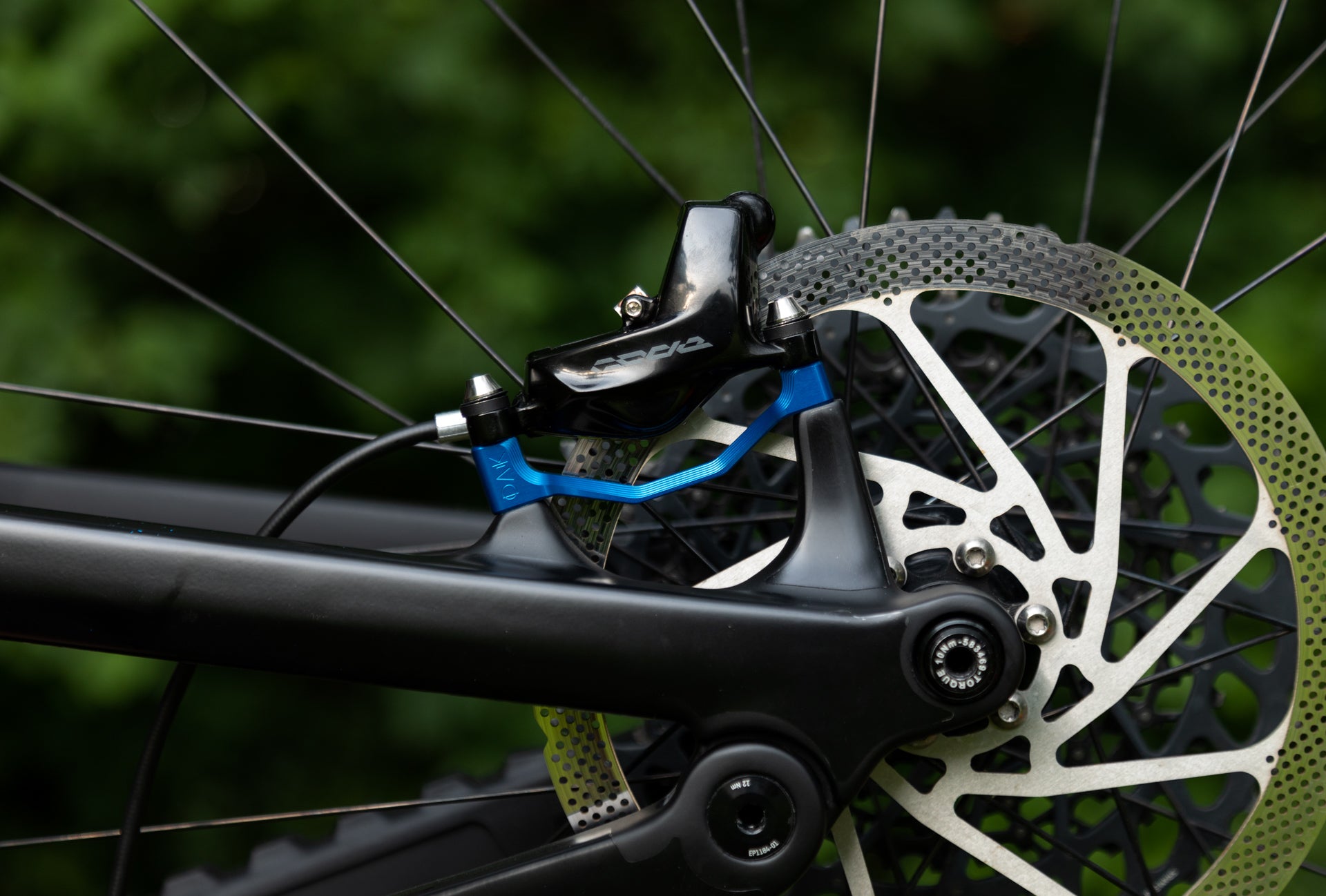 Close-up of a black rear bicycle disc brake caliper with white branding, blue adapter, and silver rotor.