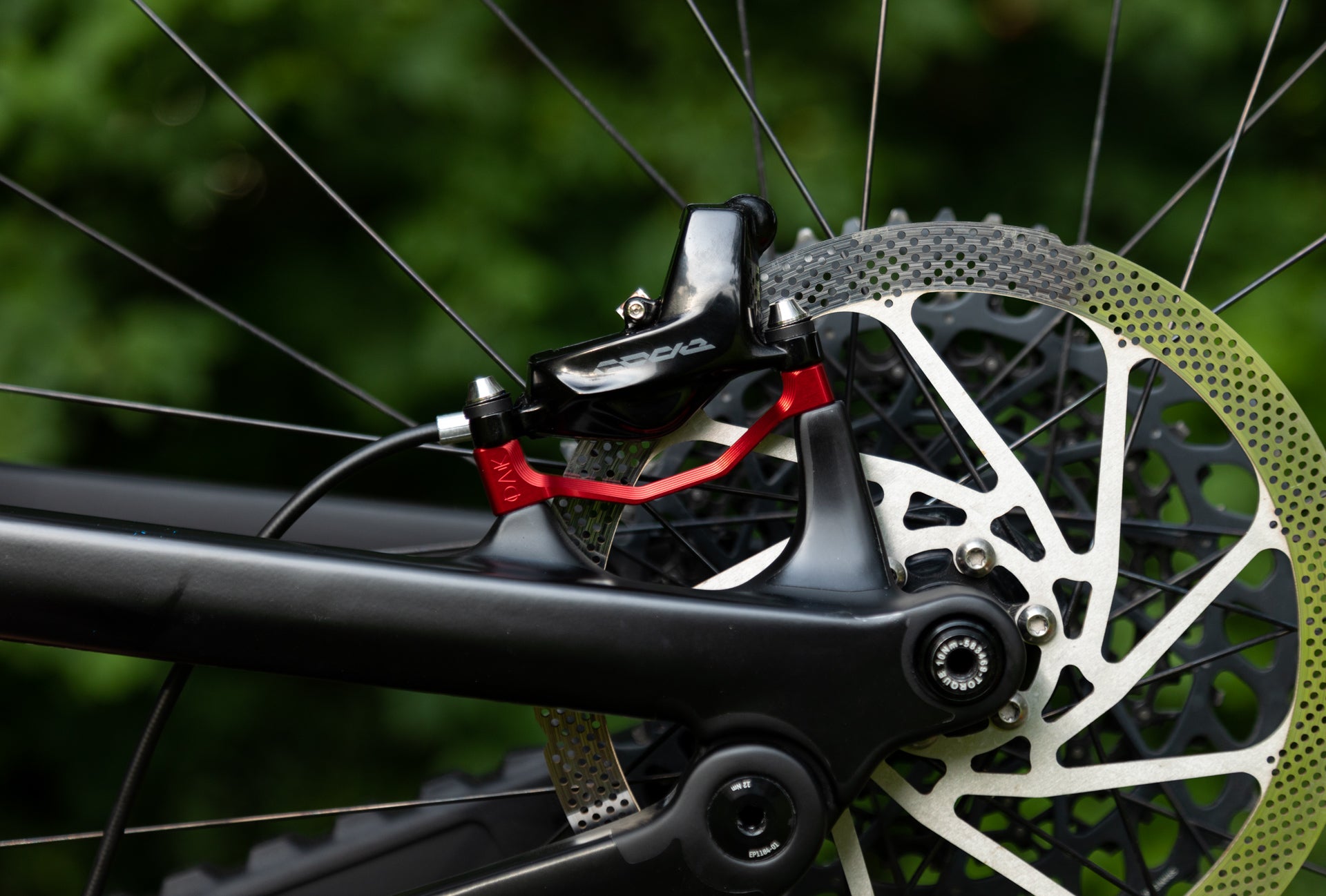 Close-up of a mountain bike's rear disc brake with red caliper and silver rotor on a black frame.