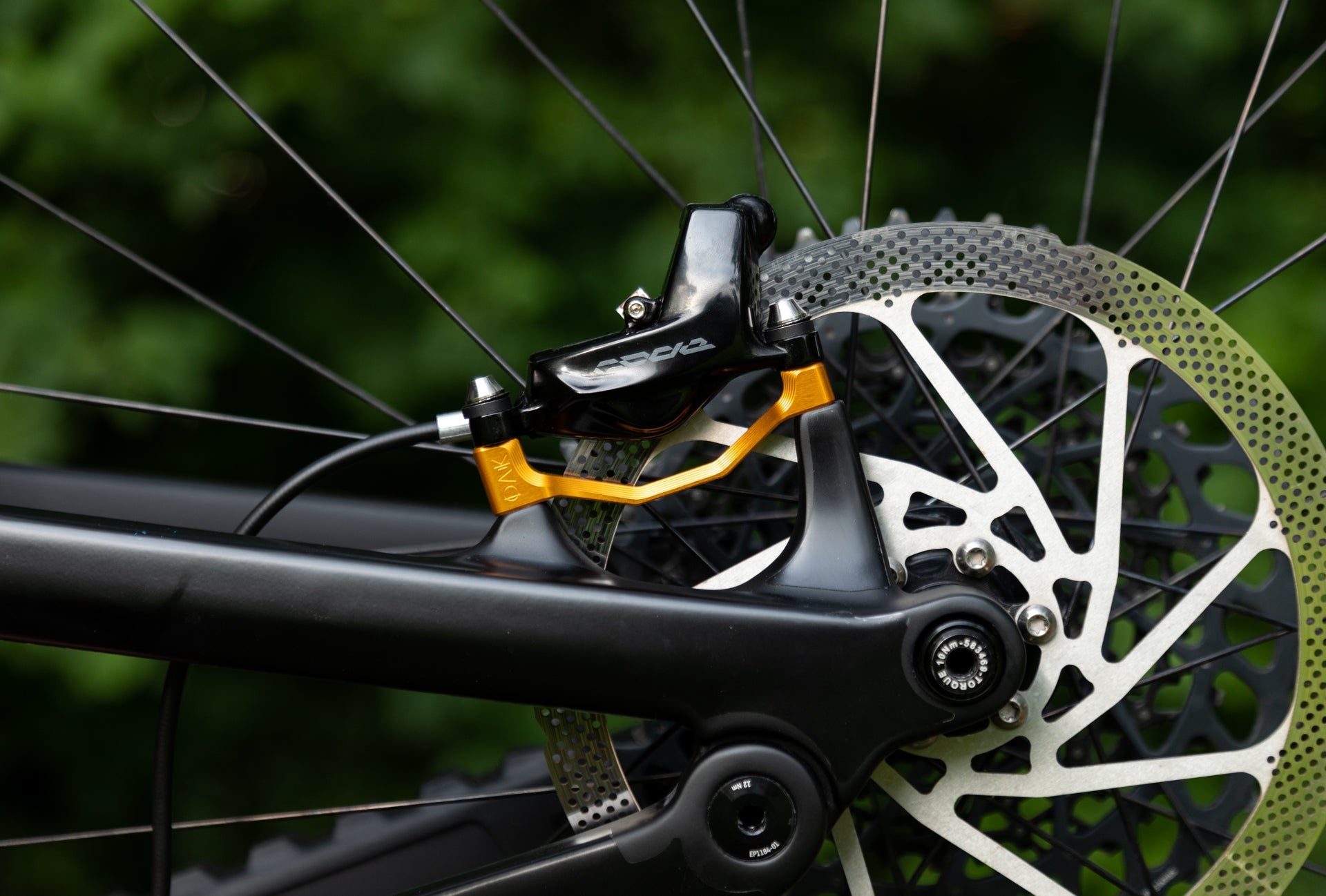 Close-up of mountain bike rear disc brake with perforated rotor, black caliper, and gold bracket