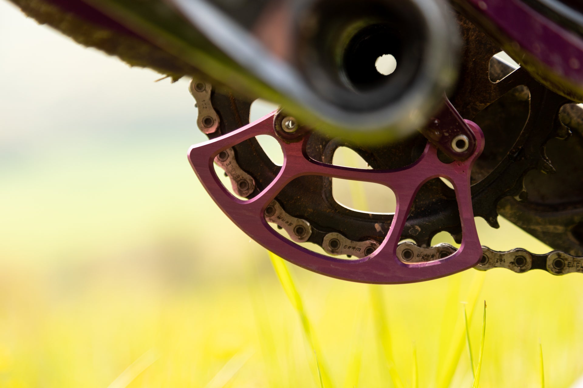 Close-up of SRAM Eagle purple chain guide on mountain bike drivetrain with chain and crankset.