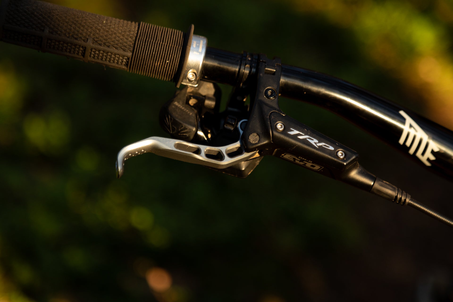 Close-up of mountain bike handlebar with black grip, TRP DH-R brake lever, and adjustment mechanism.
