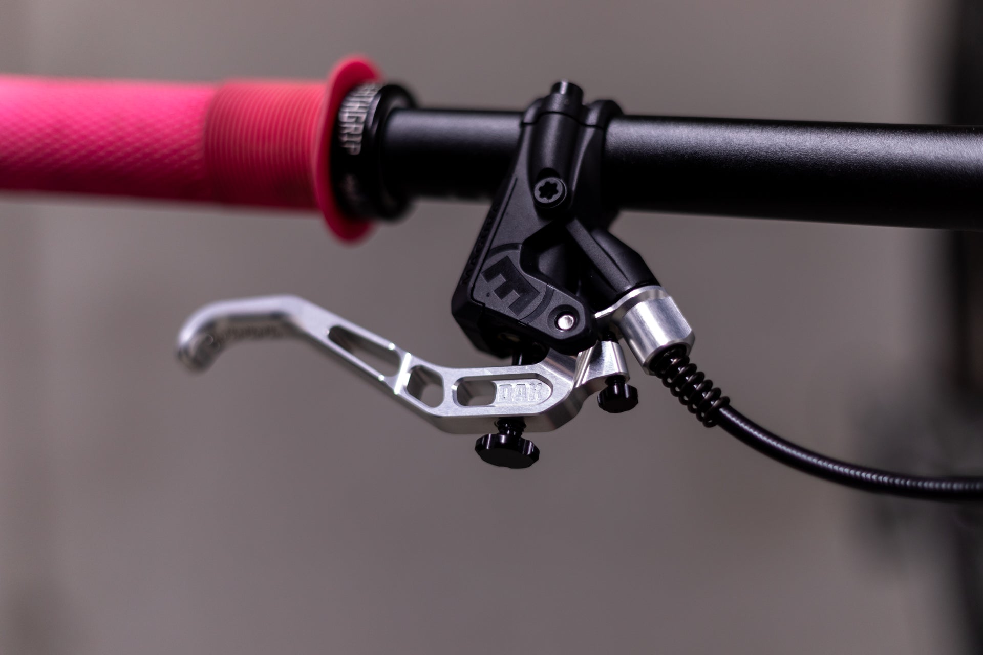 Black bicycle handlebar with pink ODI Highland grip and HOPE brake lever with JAB engraving.