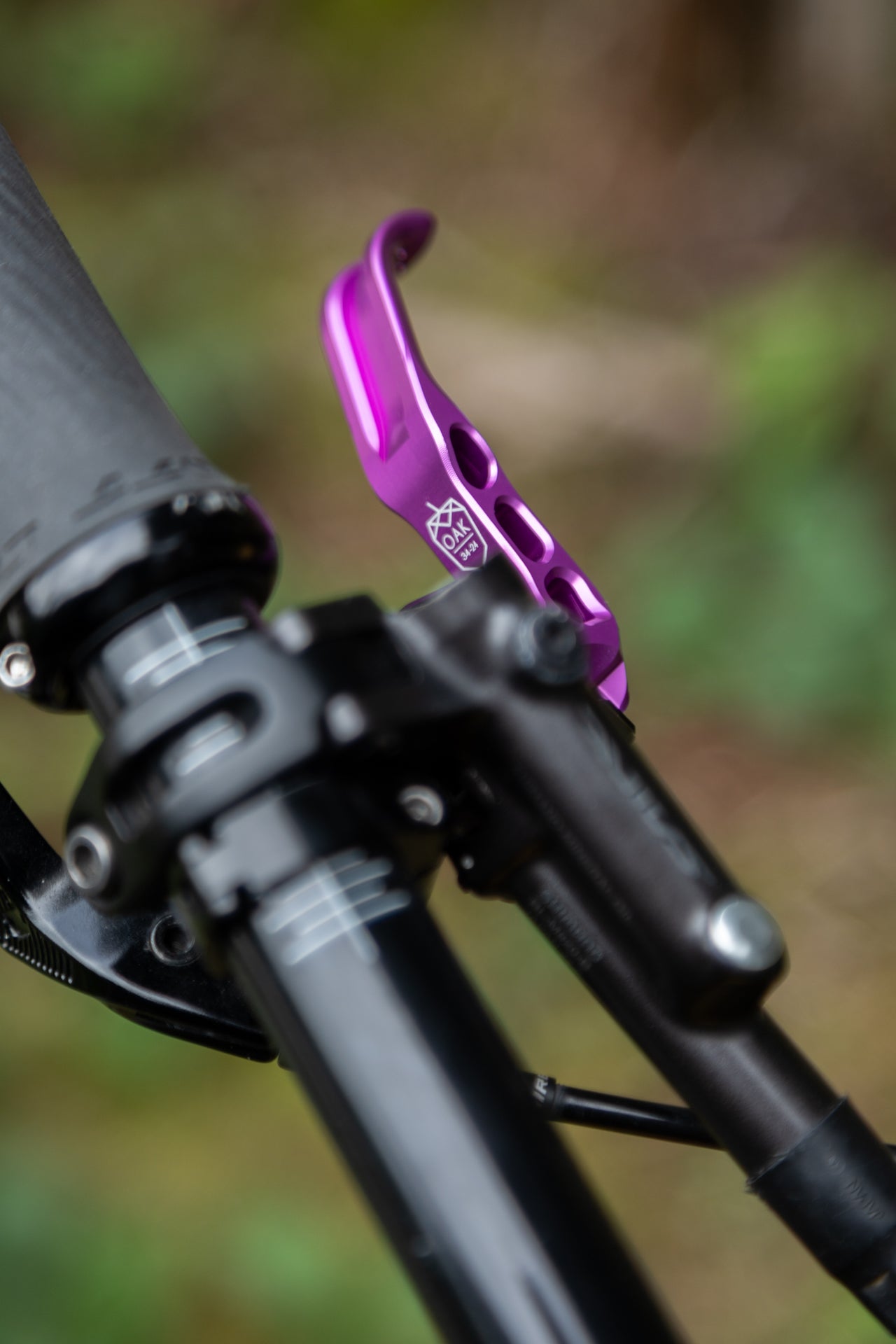 Purple mountain bike gear lever marked 'OAK 34-24' next to black handlebar grip outdoors