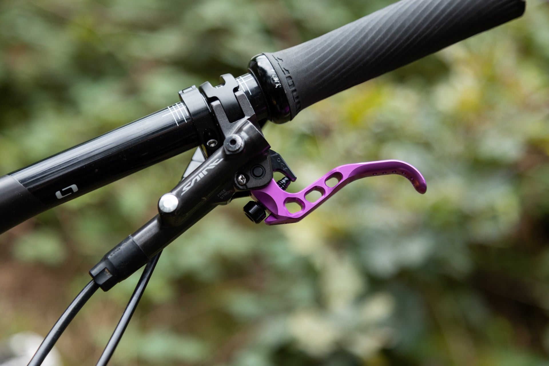 Close-up of a mountain bike handlebar with black grip and a purple anodized brake lever labeled 'FREE STROKE', outdoors.
