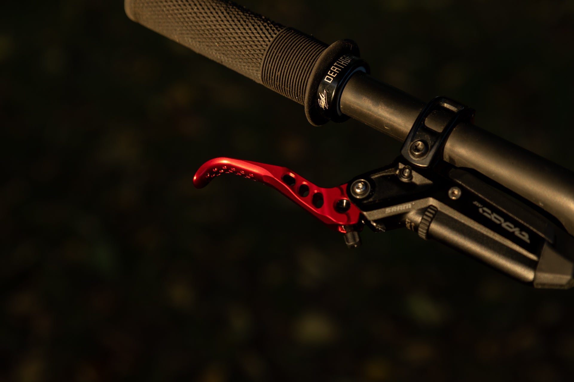 Close-up of a black textured DEATHGRIP handlebar grip and red SRAM LEVEL CODE 4 brake lever on a mountain bike.