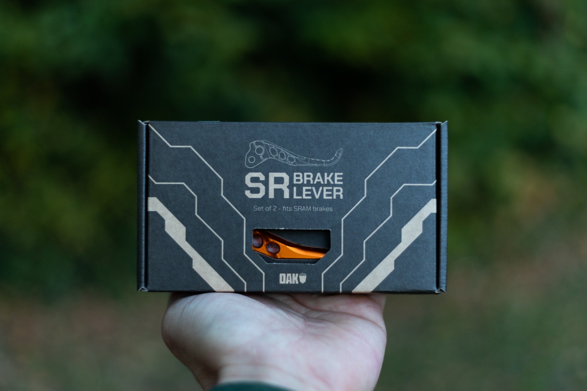 Hand holding a black box with beige circuit patterns containing two orange SR brake levers for SRAM brakes.