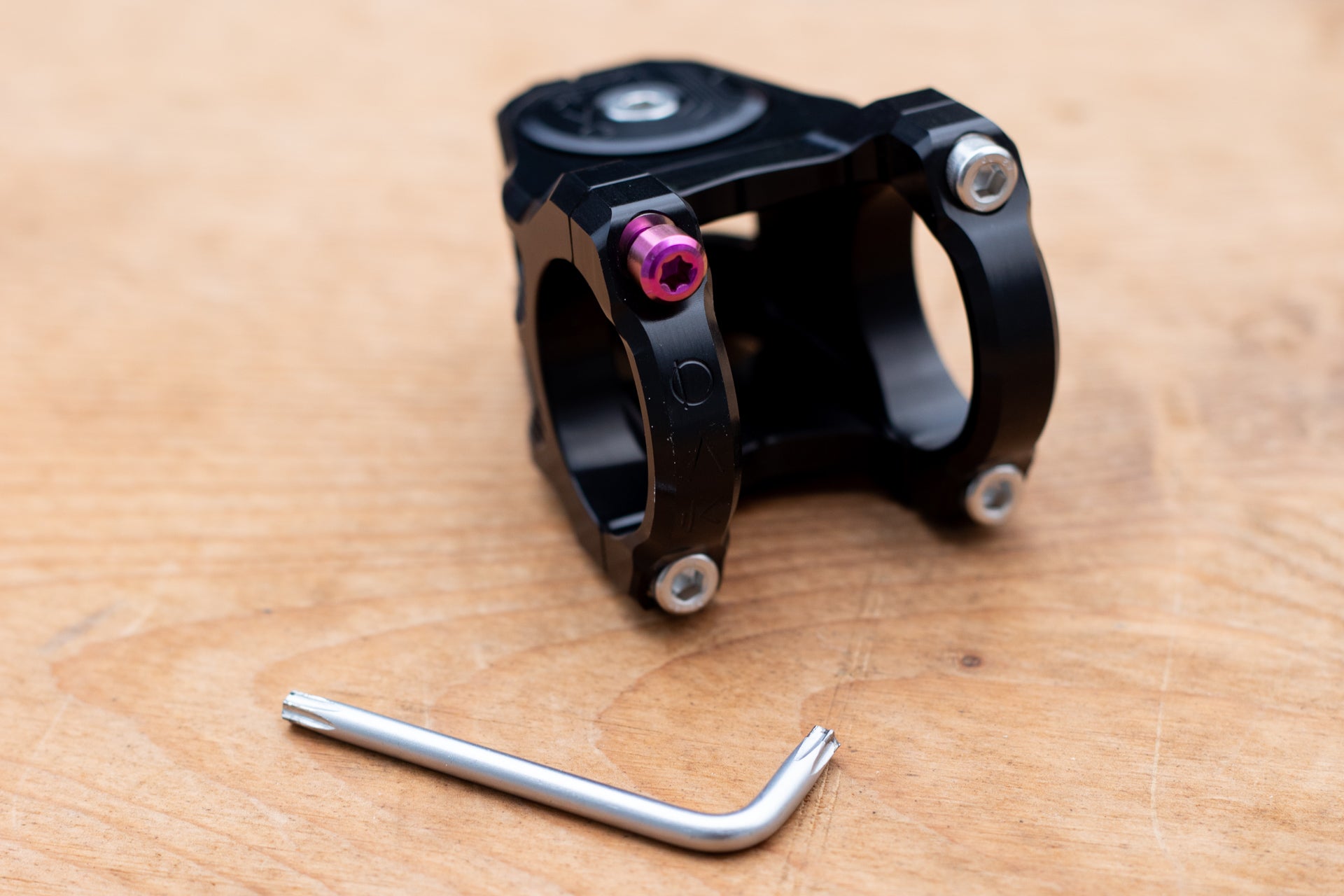 Black OX clamp with circular openings and four bolts, including a purple star bolt, on wood surface with L-shaped tool.