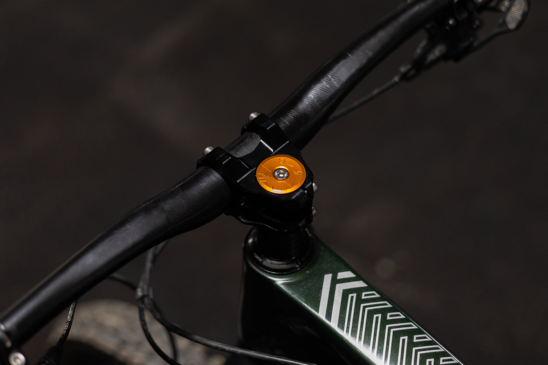 Black bicycle handlebar with an orange FORTY cap and silver bolt on a green frame with white patterns.