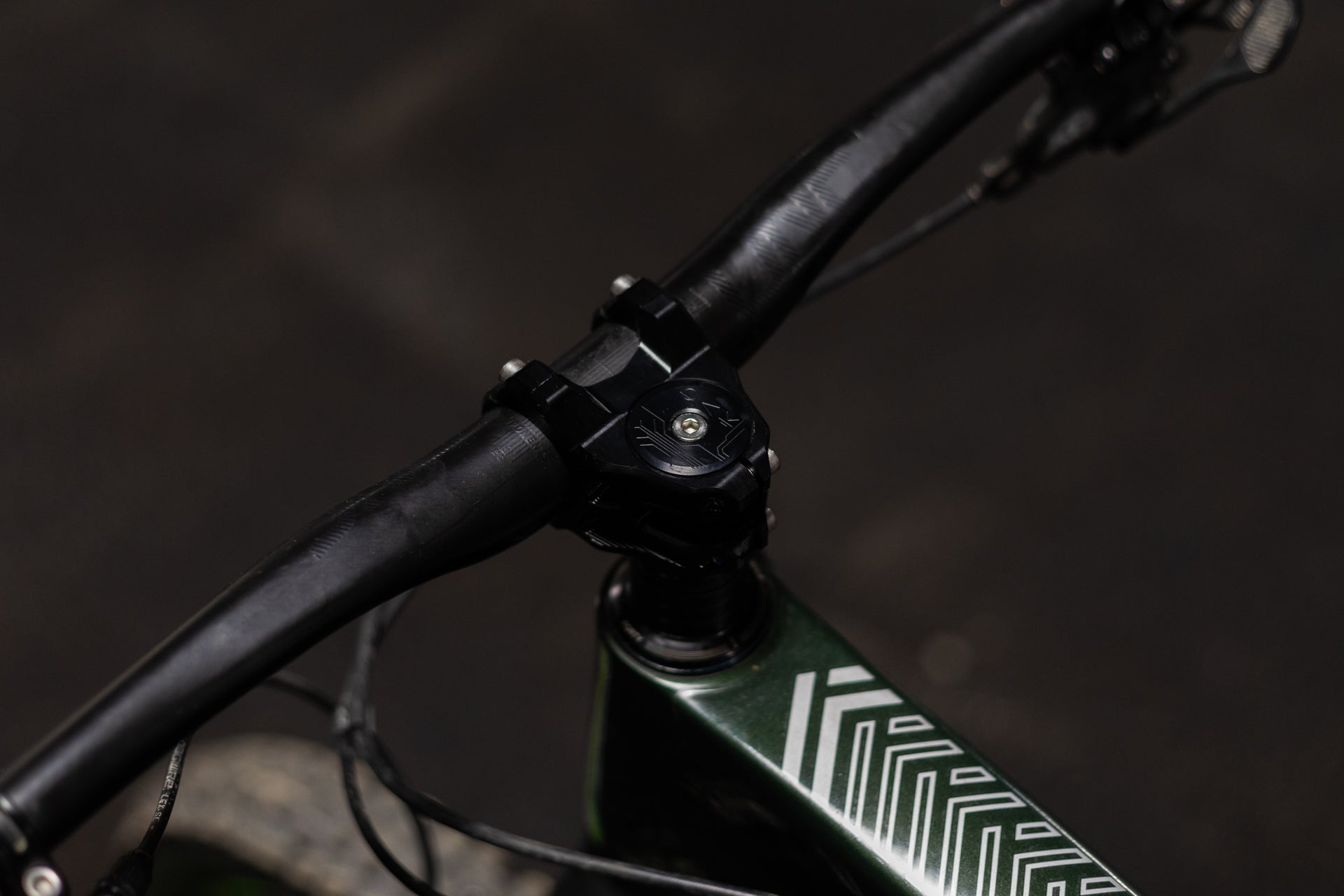 Close-up of black matte ROK bicycle handlebar mounted on dark green frame with white geometric lines and silver bolts