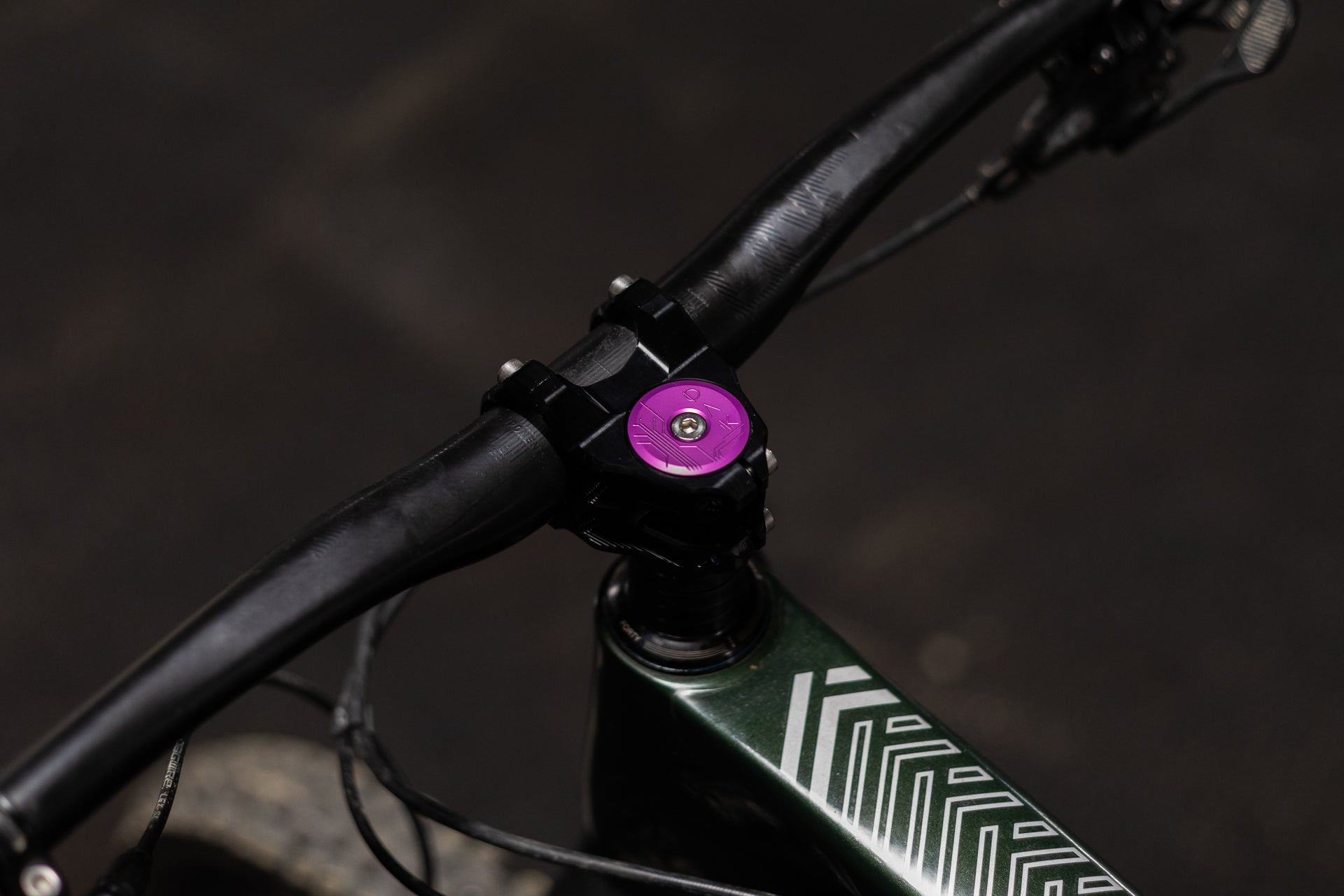 Black mountain bike handlebar with purple FORTY top cap and dark green frame with white geometric patterns
