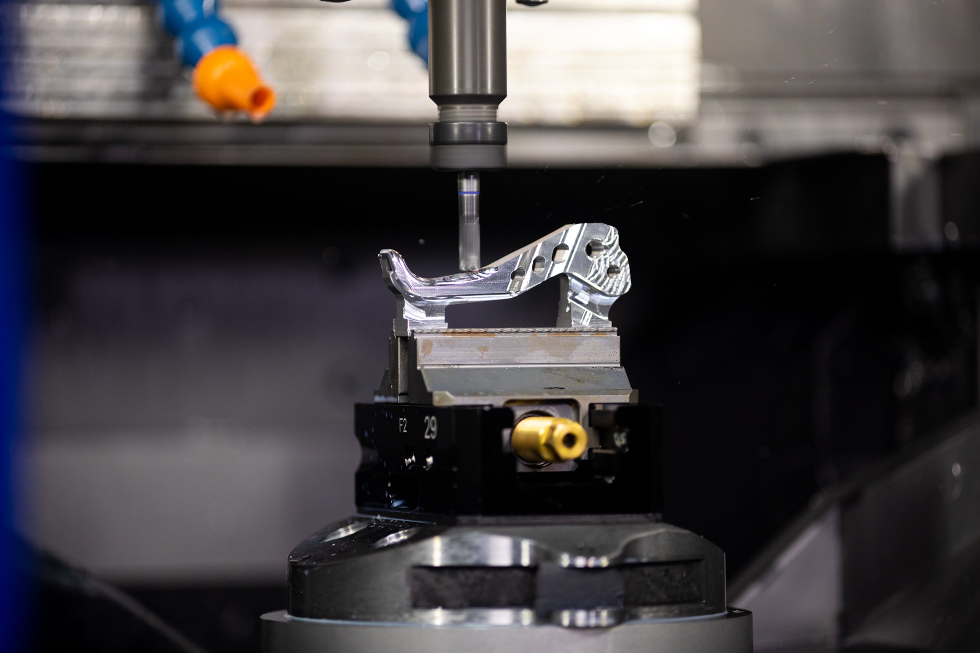 Close-up of a metallic bike part labeled F2 29 being machined by a vertical milling tool