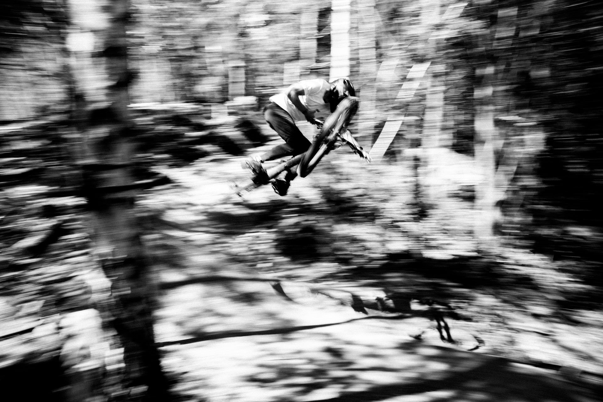 Mountain biker executing an airborne jump in a forest, demonstrating speed and control.