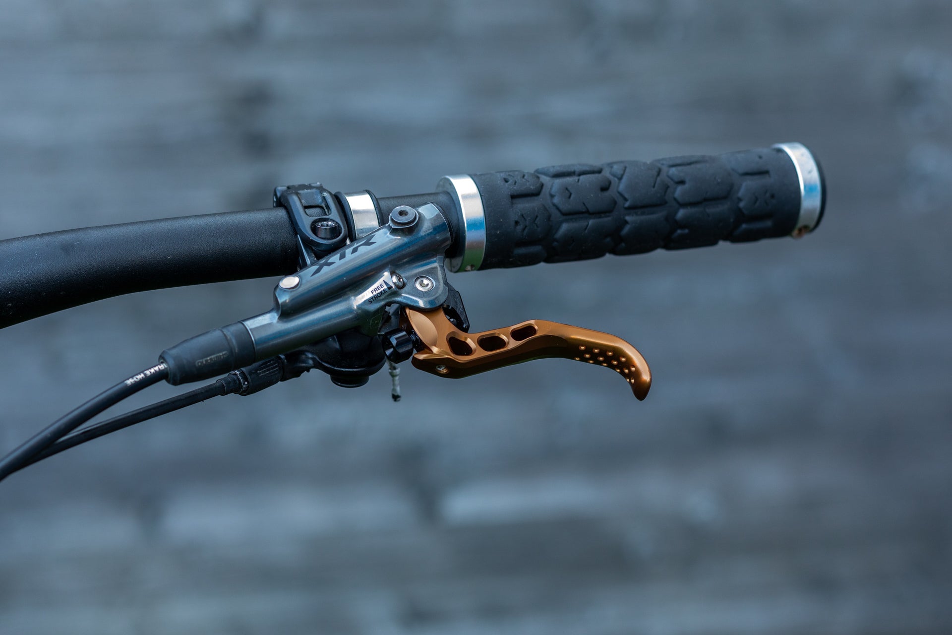 Close-up of black mountain bike handlebar with textured grip and bronze perforated brake lever.