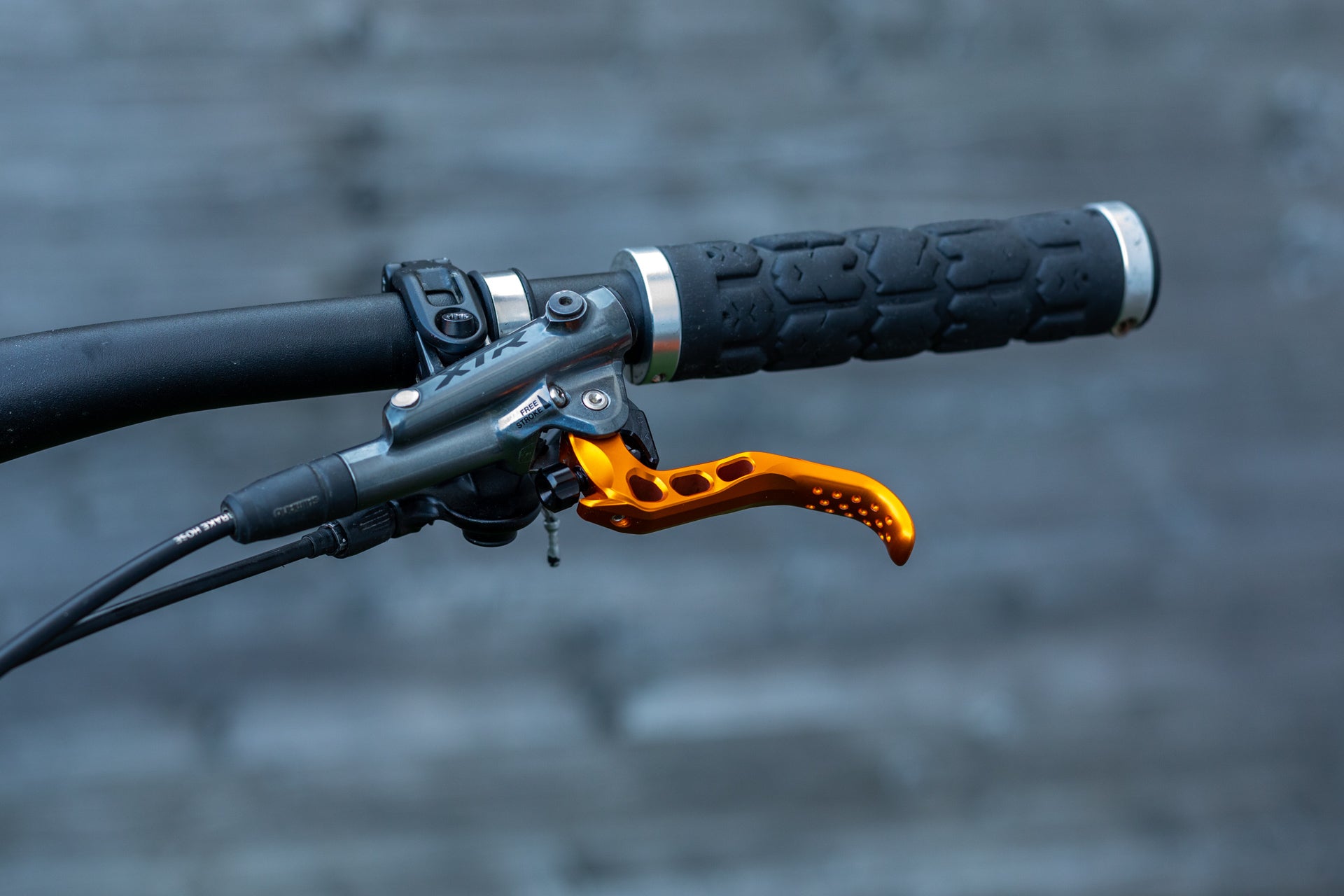 Close-up of mountain bike handlebar with black grip and orange ergonomic brake lever with cut-out holes