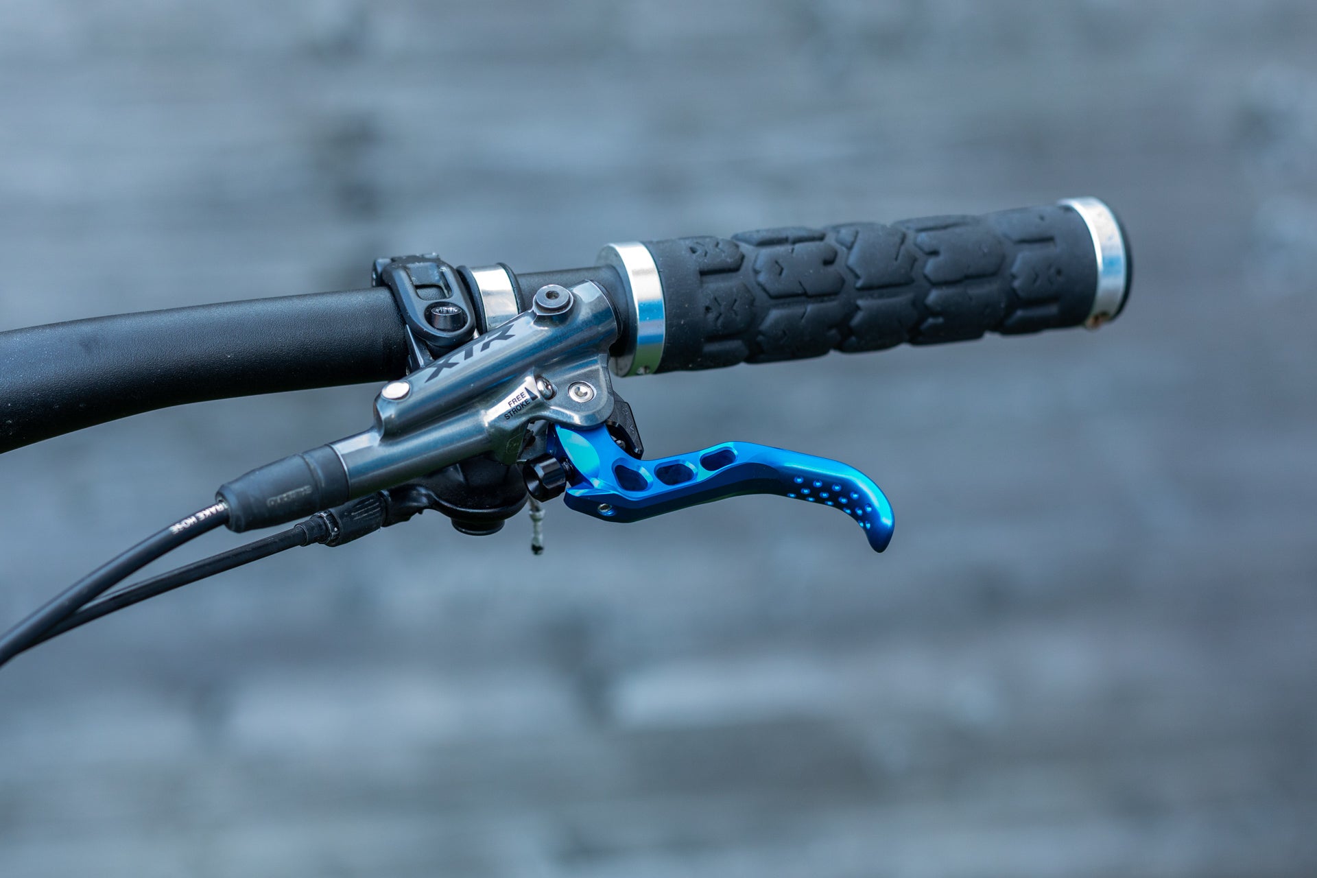 Close-up of mountain bike handlebar with black grip and metallic blue brake lever engraved 'FREE STROKE'.
