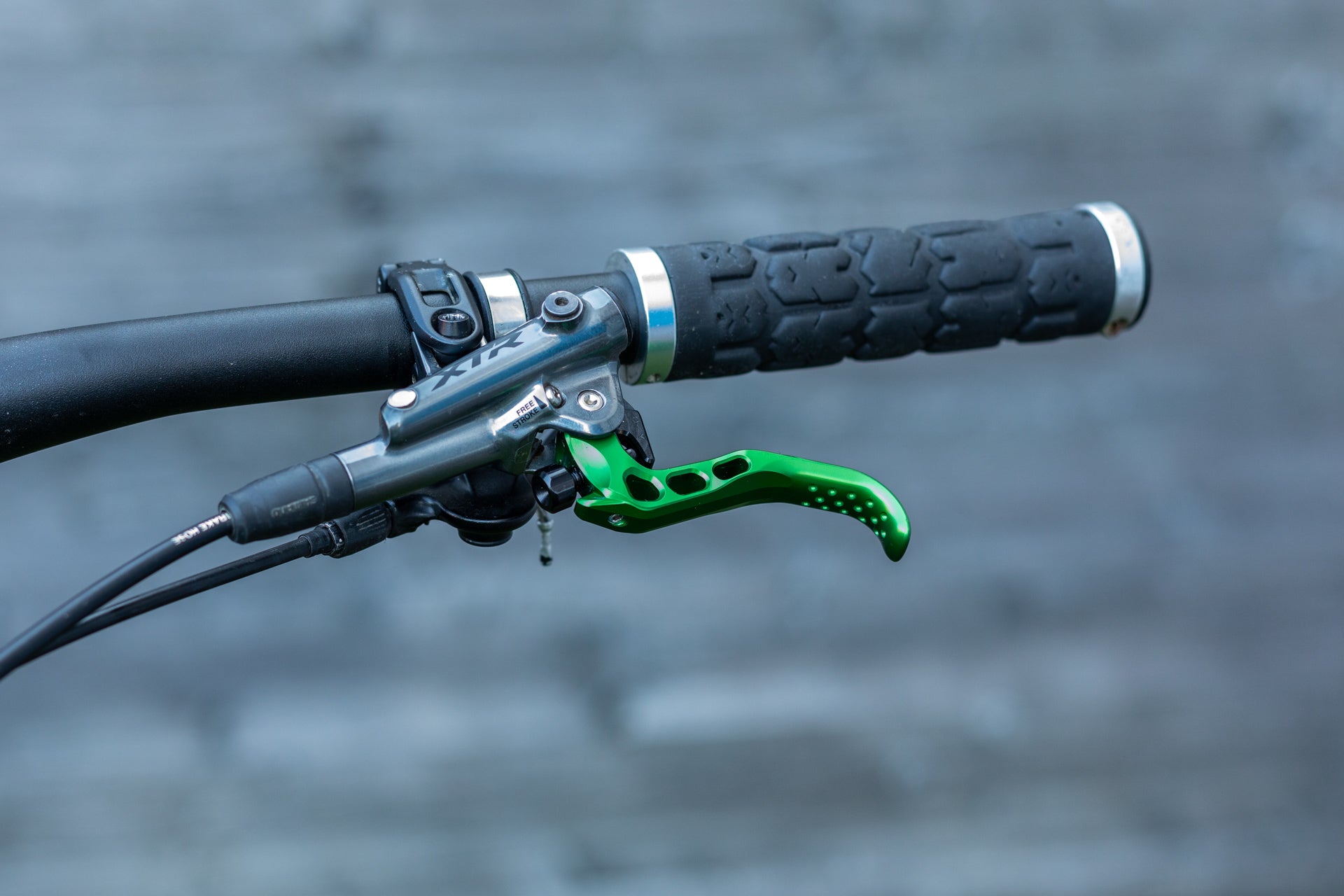 Close-up of a mountain bike handlebar grip and green XTR brake lever on a gray background.