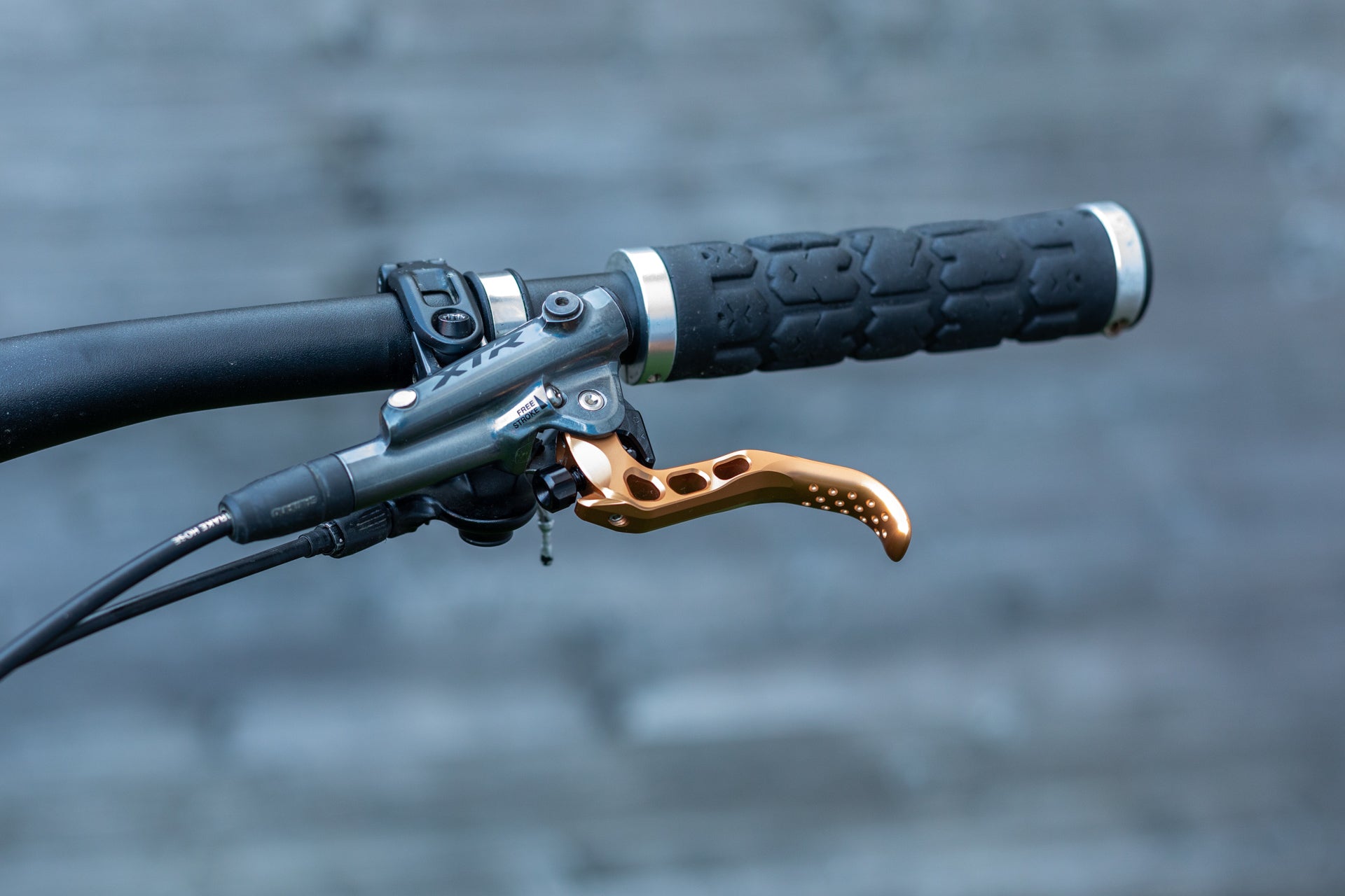 Mountain bike handlebar with black grip, gold XTR brake lever, and Free Stroke housing on gray background.