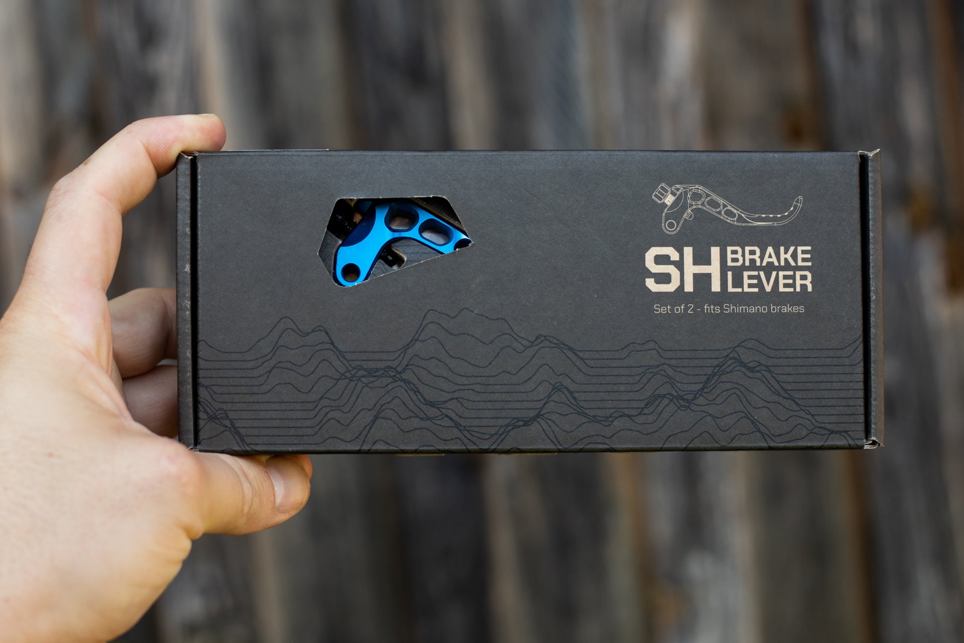 Black packaging displaying blue metallic Shimano brake lever parts on a wooden background.