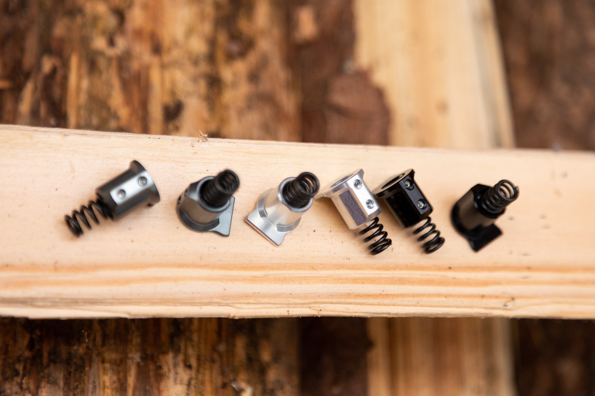 Six silver, gray, and black cylindrical metal springs on a light wooden plank, dark wood background.