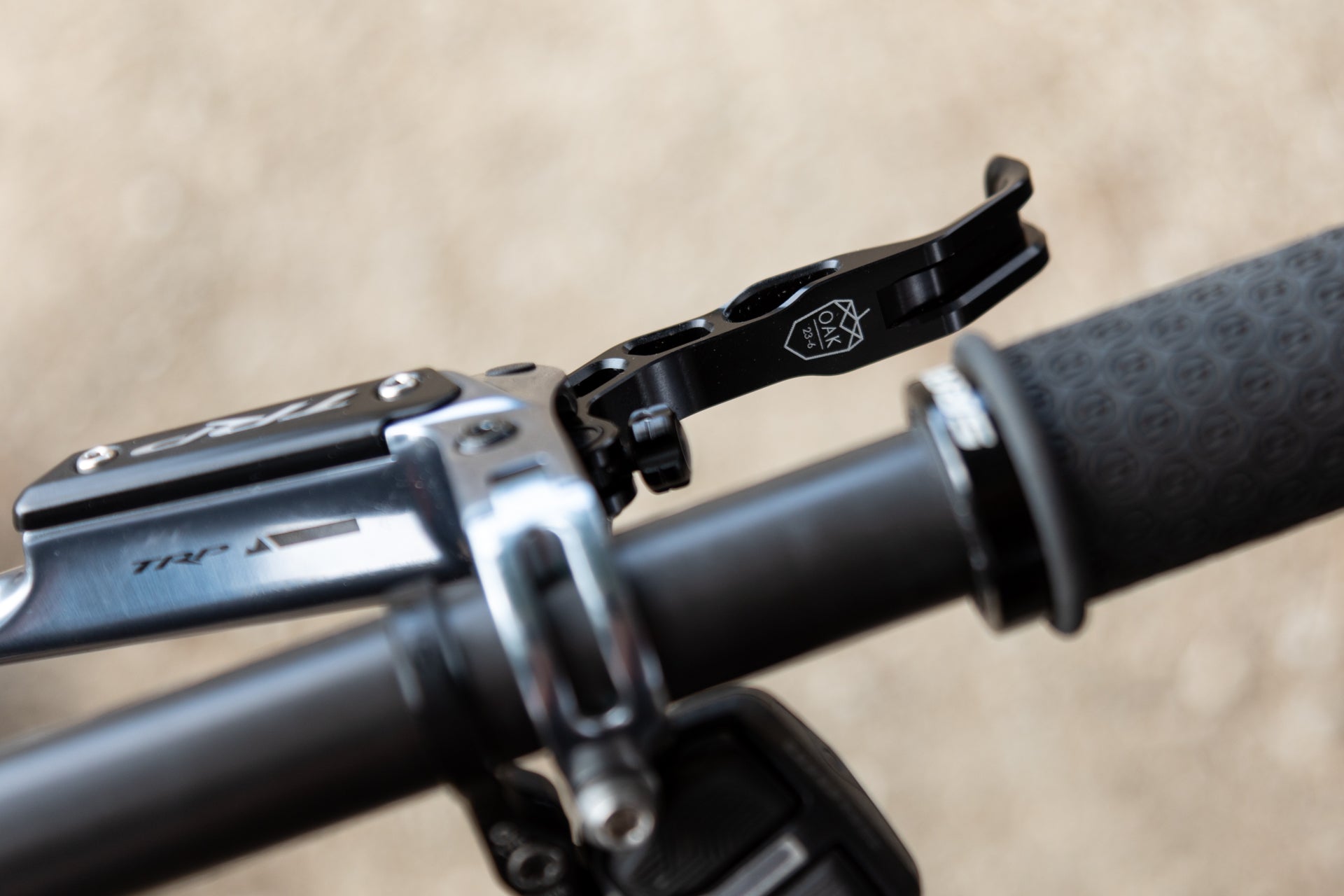 Close-up of black OAK 23-6 bicycle brake lever on handlebar with textured grip, beige background