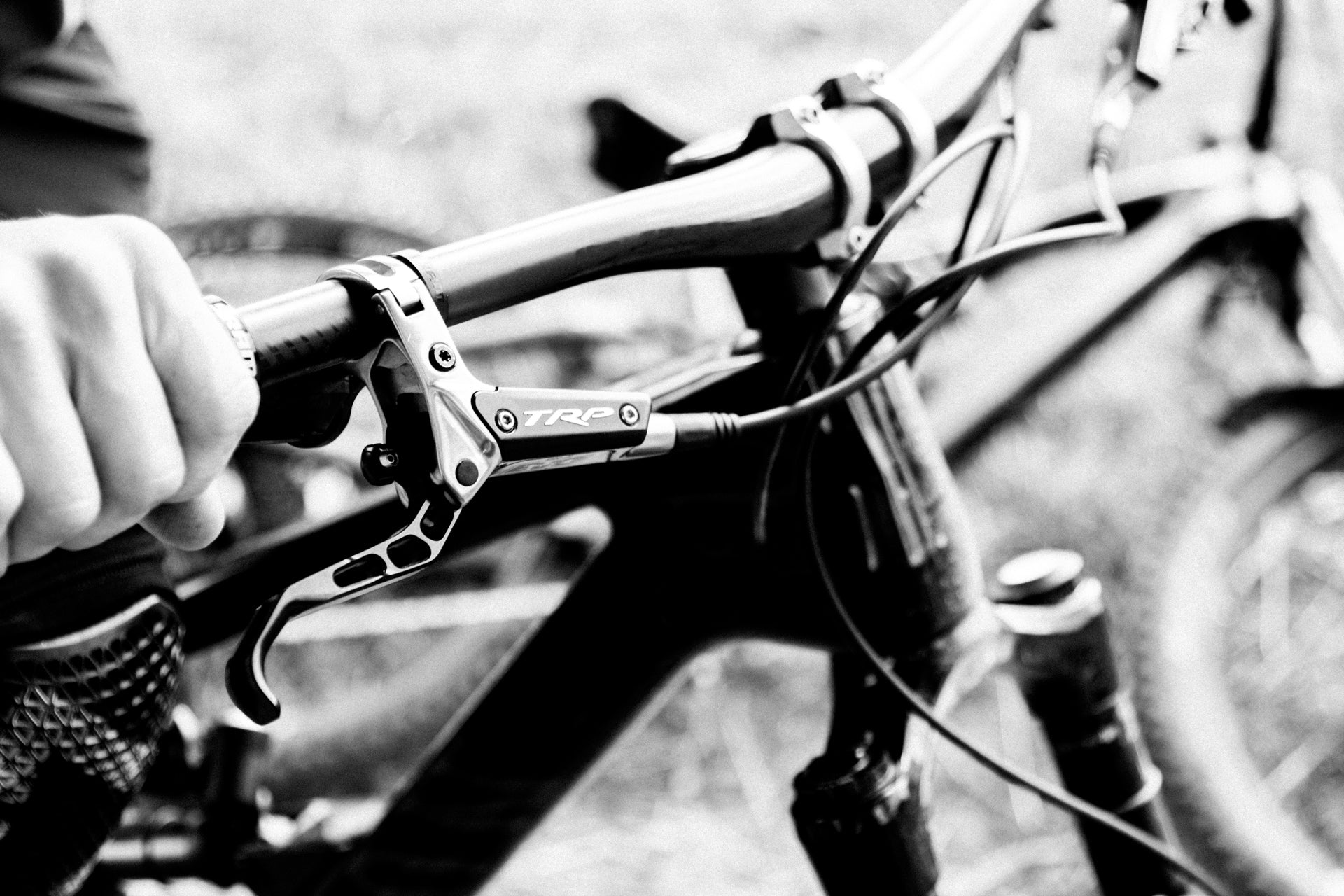 Close-up of a mountain bike handlebar with TRP brake lever and gloved hand, outdoors.