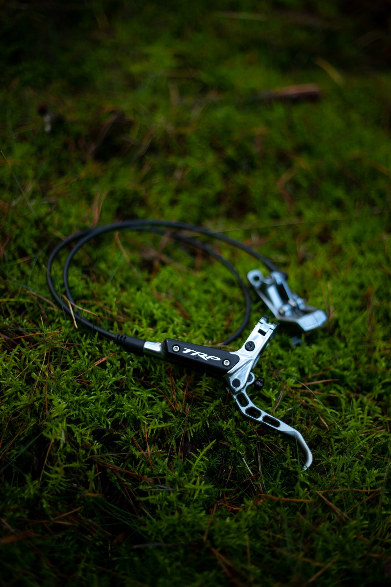 Black and silver TRP hydraulic bike brake lever on green moss with attached cable