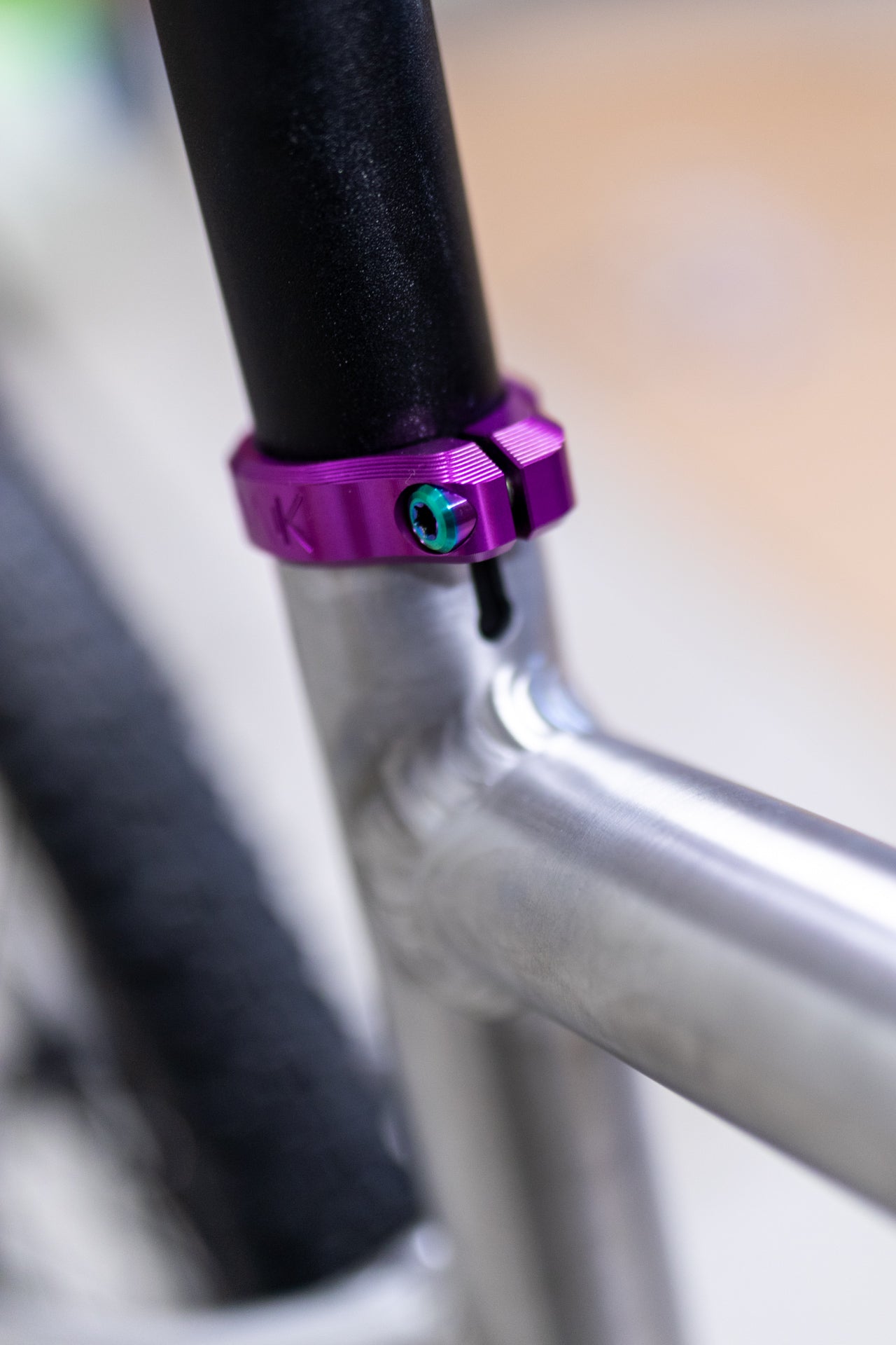 Metallic purple bicycle seat post clamp with teal bolt on a silver frame with precise welds and engraved K.