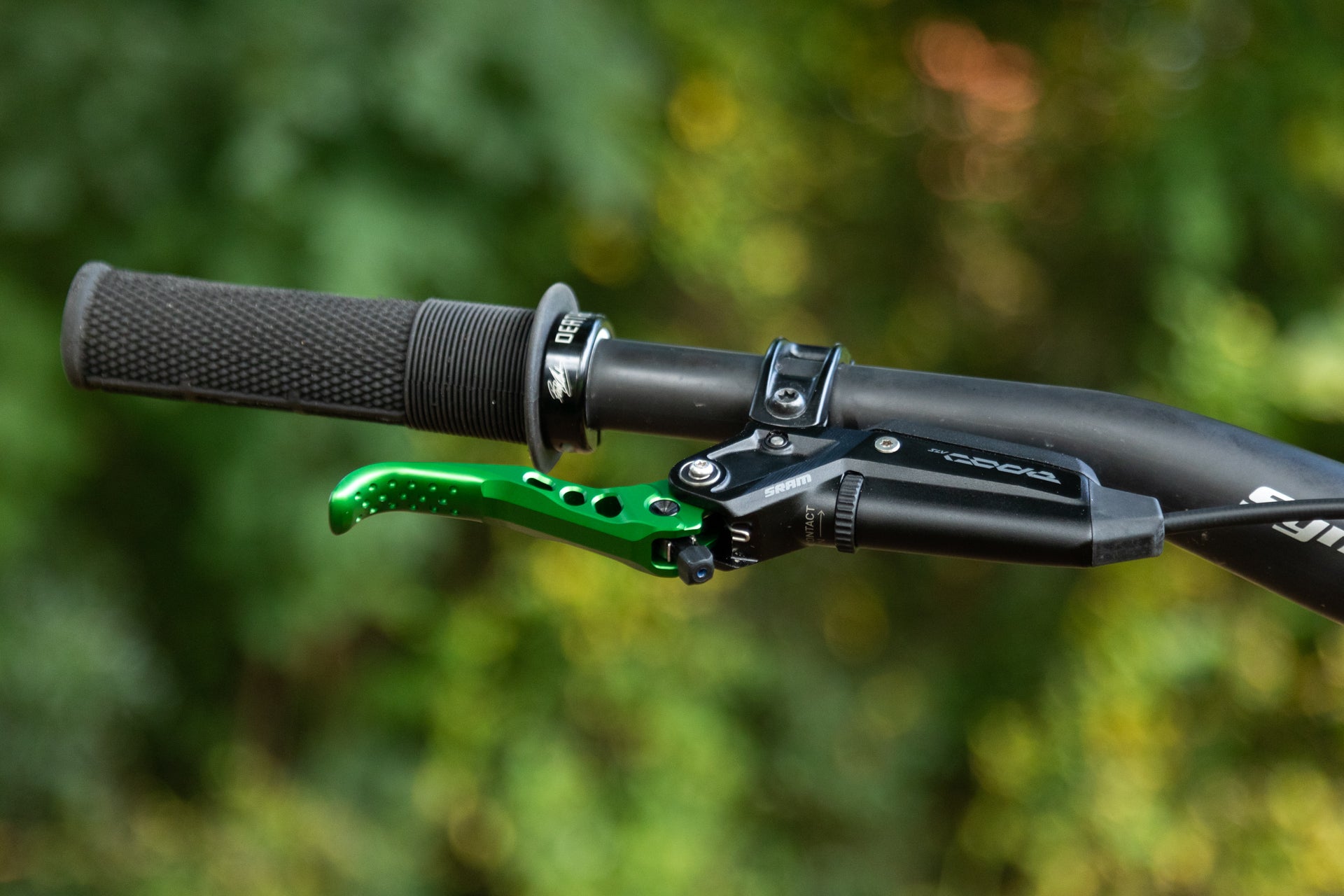 Close-up of a black textured bicycle handlebar grip with a green metallic SRAM brake lever and control housing.