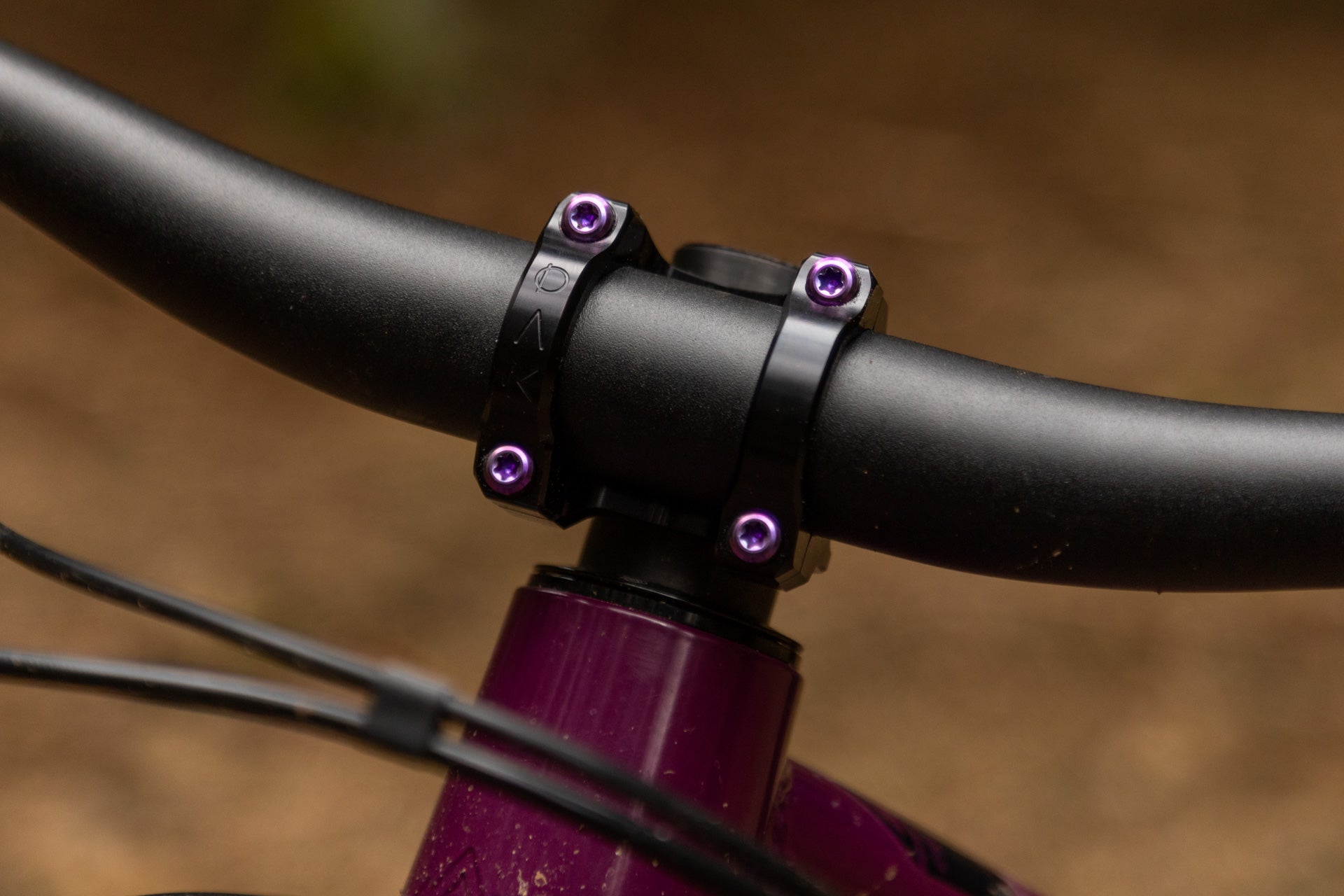 Close-up of black bicycle handlebar with purple screws on a purple frame head tube, showcasing bike component quality.